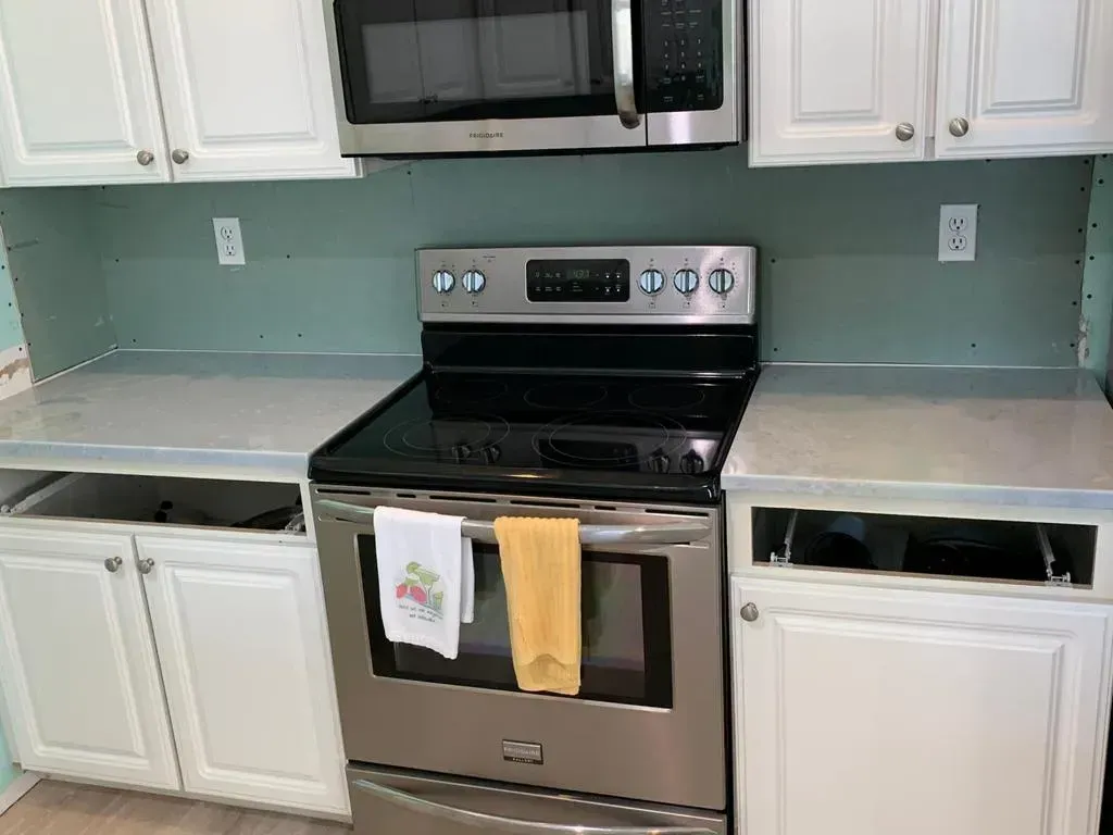 Kitchen with white cabinets, black microwave, stainless steel stove, and light green backsplash.