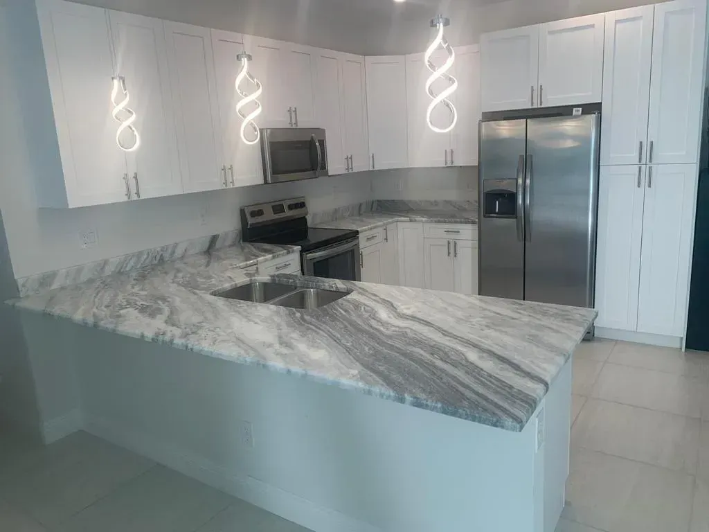Modern white kitchen with granite island, stainless steel appliances, and pendant lights