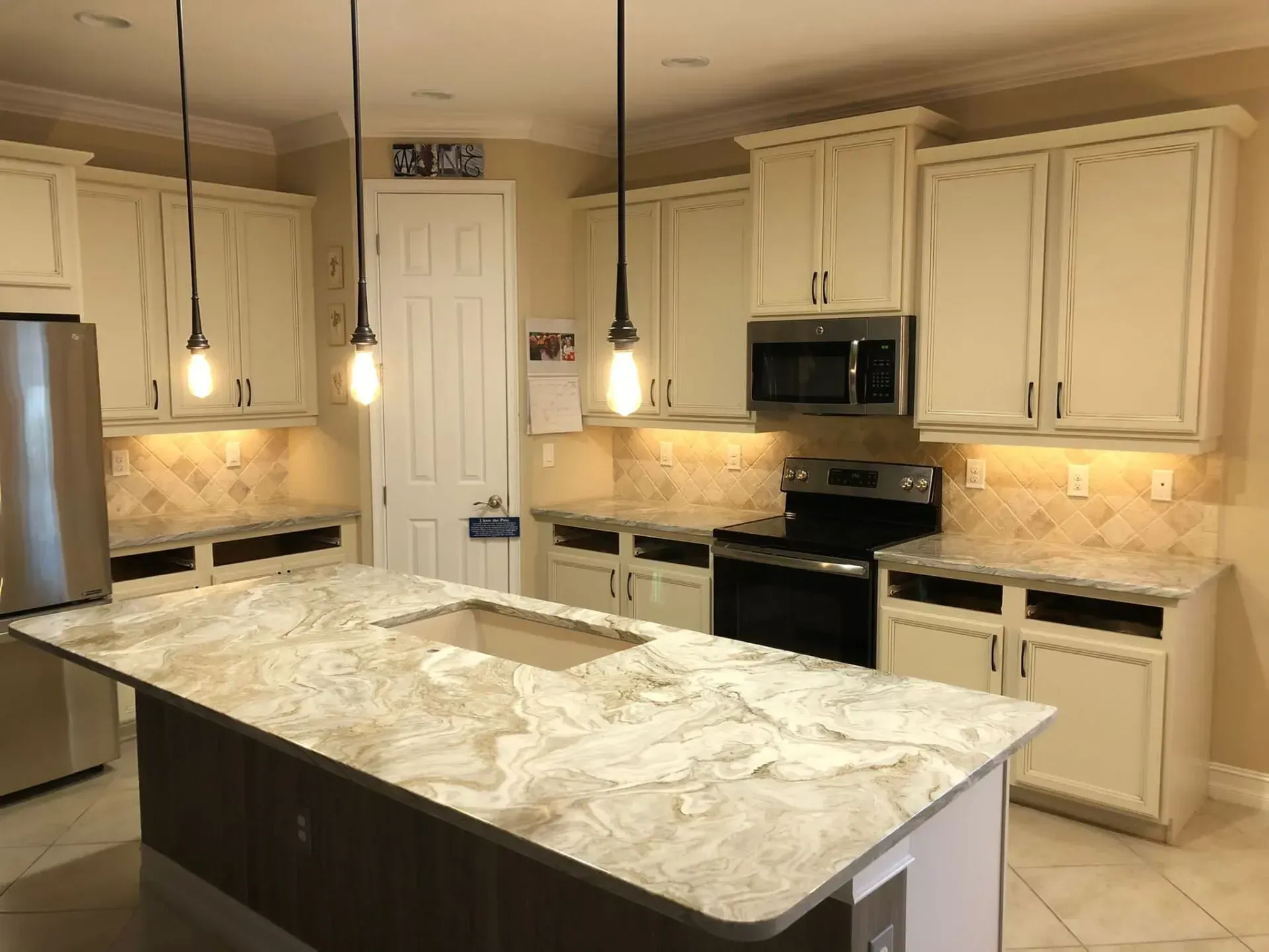 Bright kitchen with cream cabinets, granite island, pendant lights, and stainless steel appliances