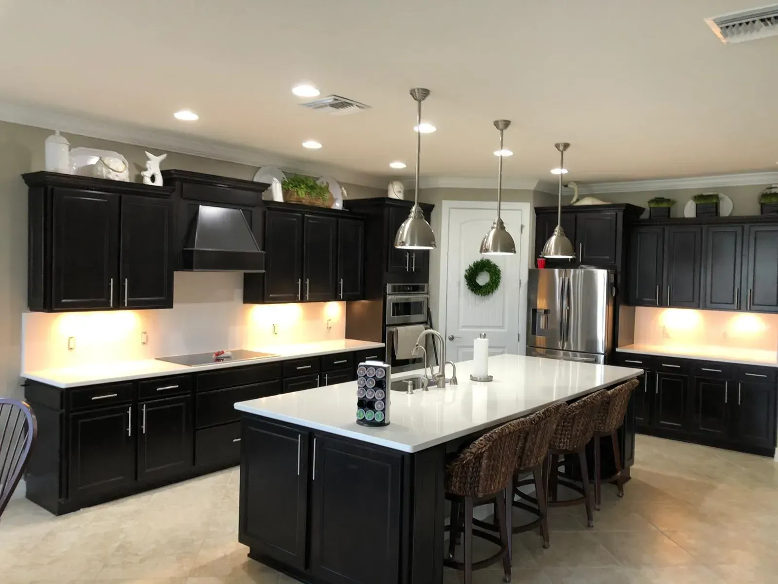 Modern kitchen with black cabinets, stainless appliances, and a white island with pendant lights