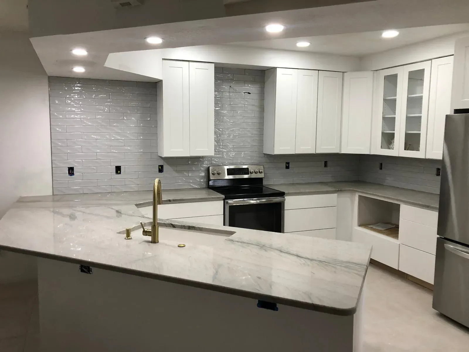 Modern white kitchen with island, stainless steel appliances, and gray tile backsplash