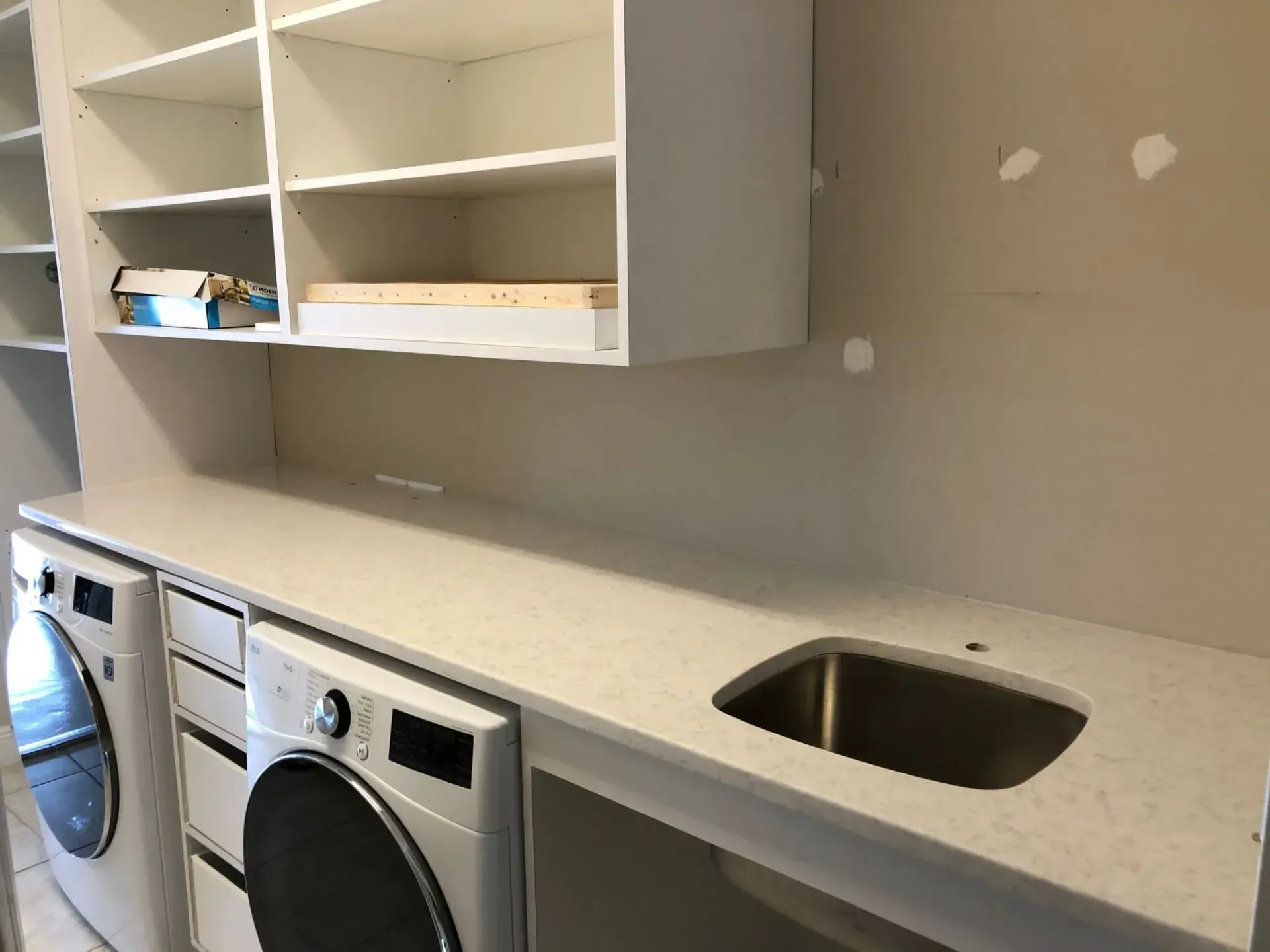 Laundry room countertop with sink and open shelves above washer and dryer units.