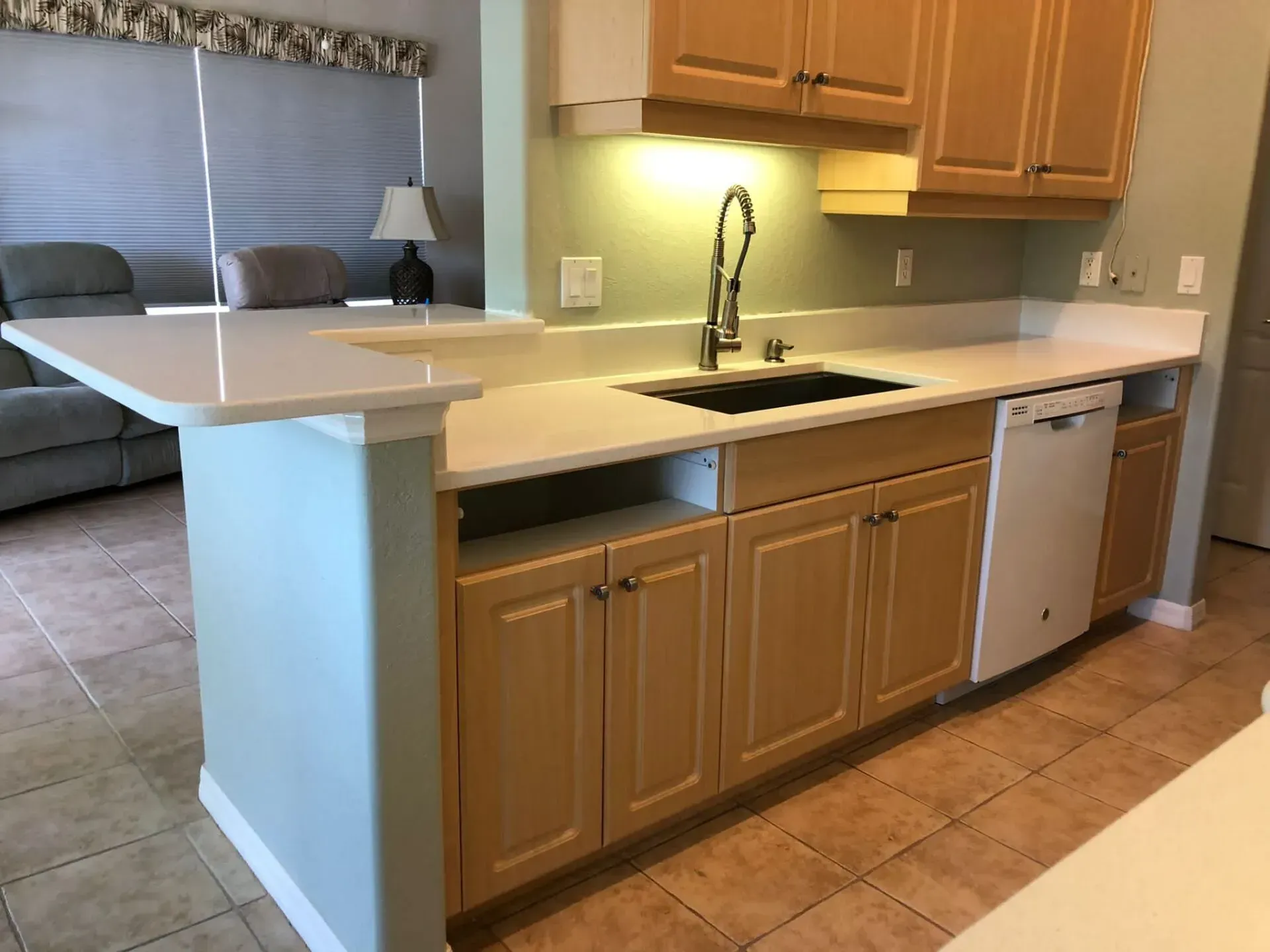 Kitchen with light wood cabinets, white countertops, sink, and a built-in breakfast bar.