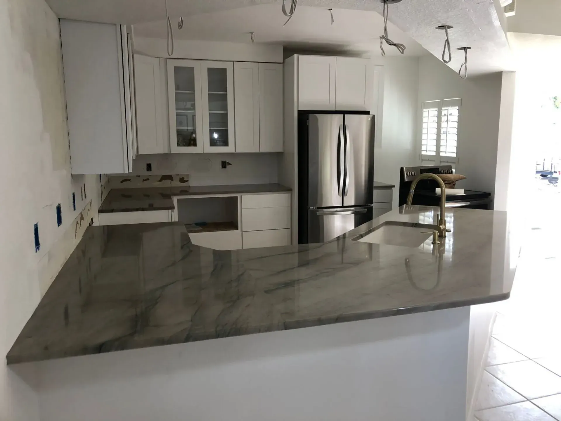 Modern kitchen with white cabinets, stainless fridge, and large gray granite island countertop