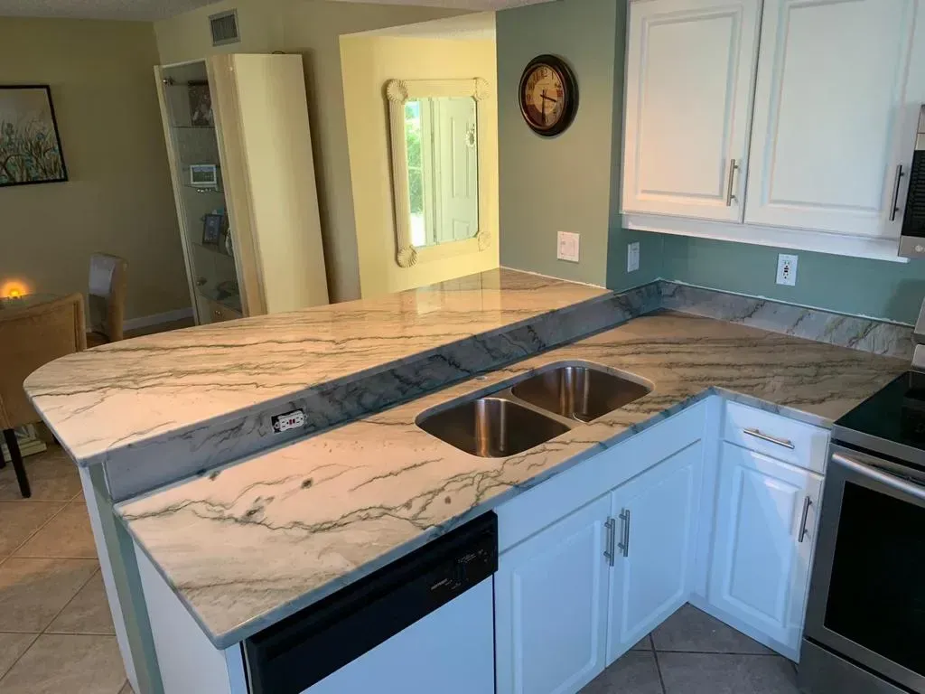 Bright kitchen with white cabinets, double sink, gray tile backsplash, and a marble-look countertop.