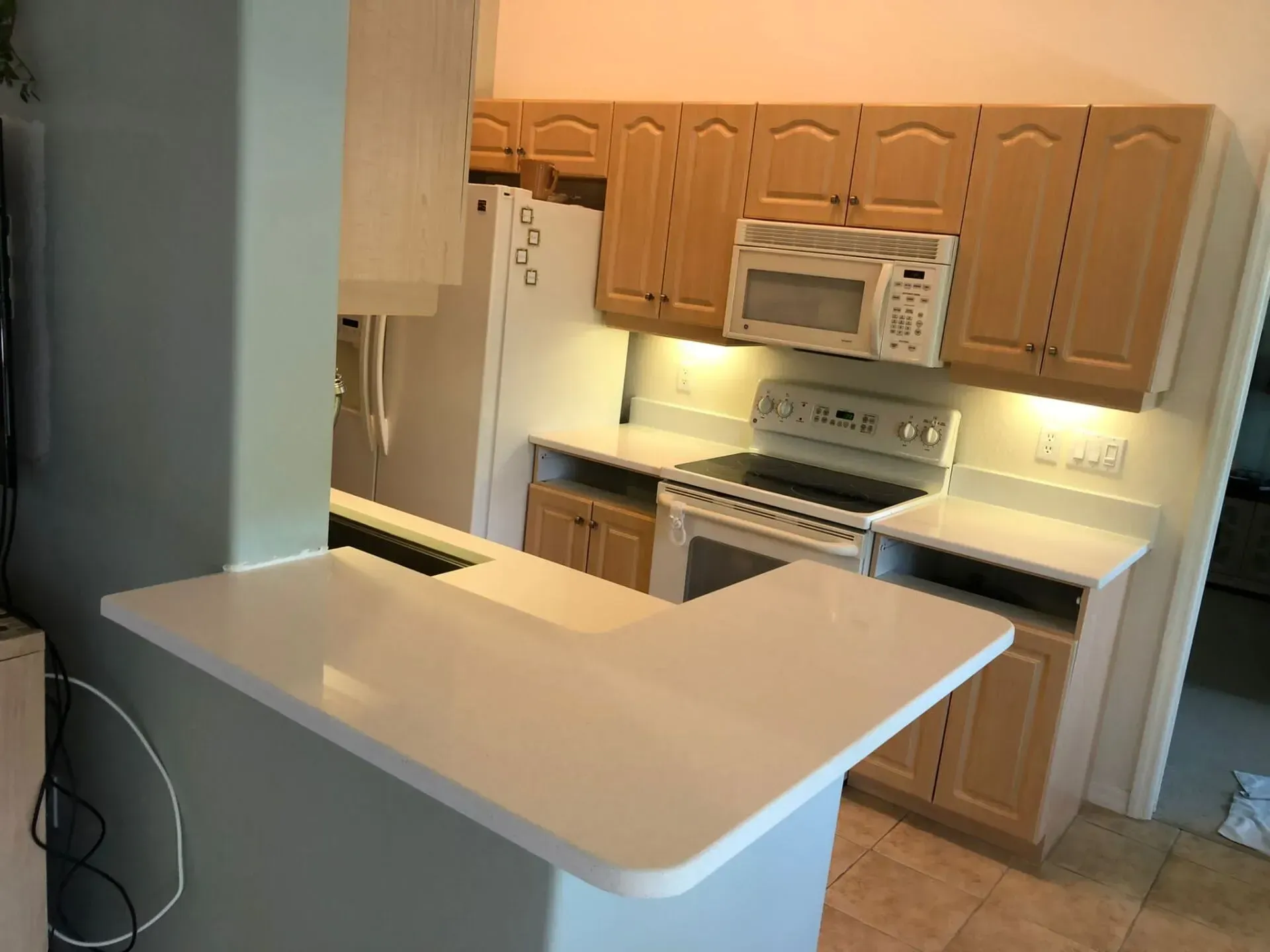 Small kitchen with light wood cabinets, white appliances, and a white breakfast bar counter.