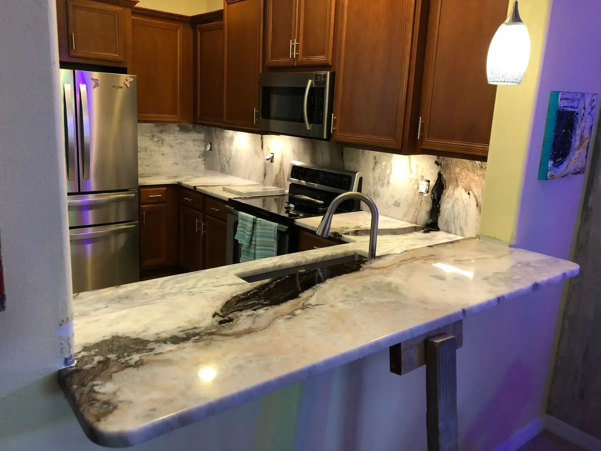 Kitchen with marble island, stainless fridge, dark wood cabinets, and pendant light.