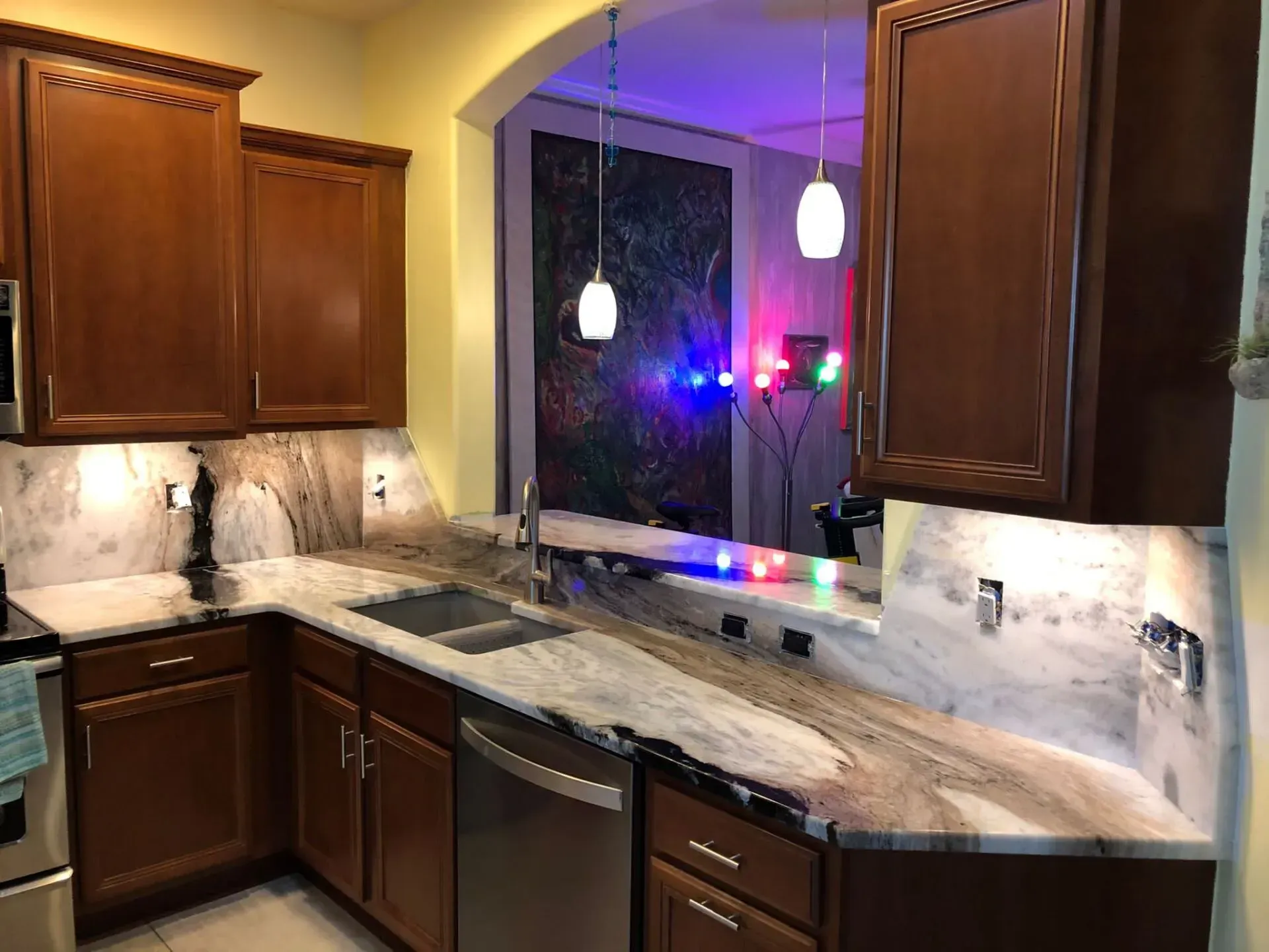 Modern kitchen with dark wood cabinets, marble countertop, and a window above the sink lit by purple and red lights