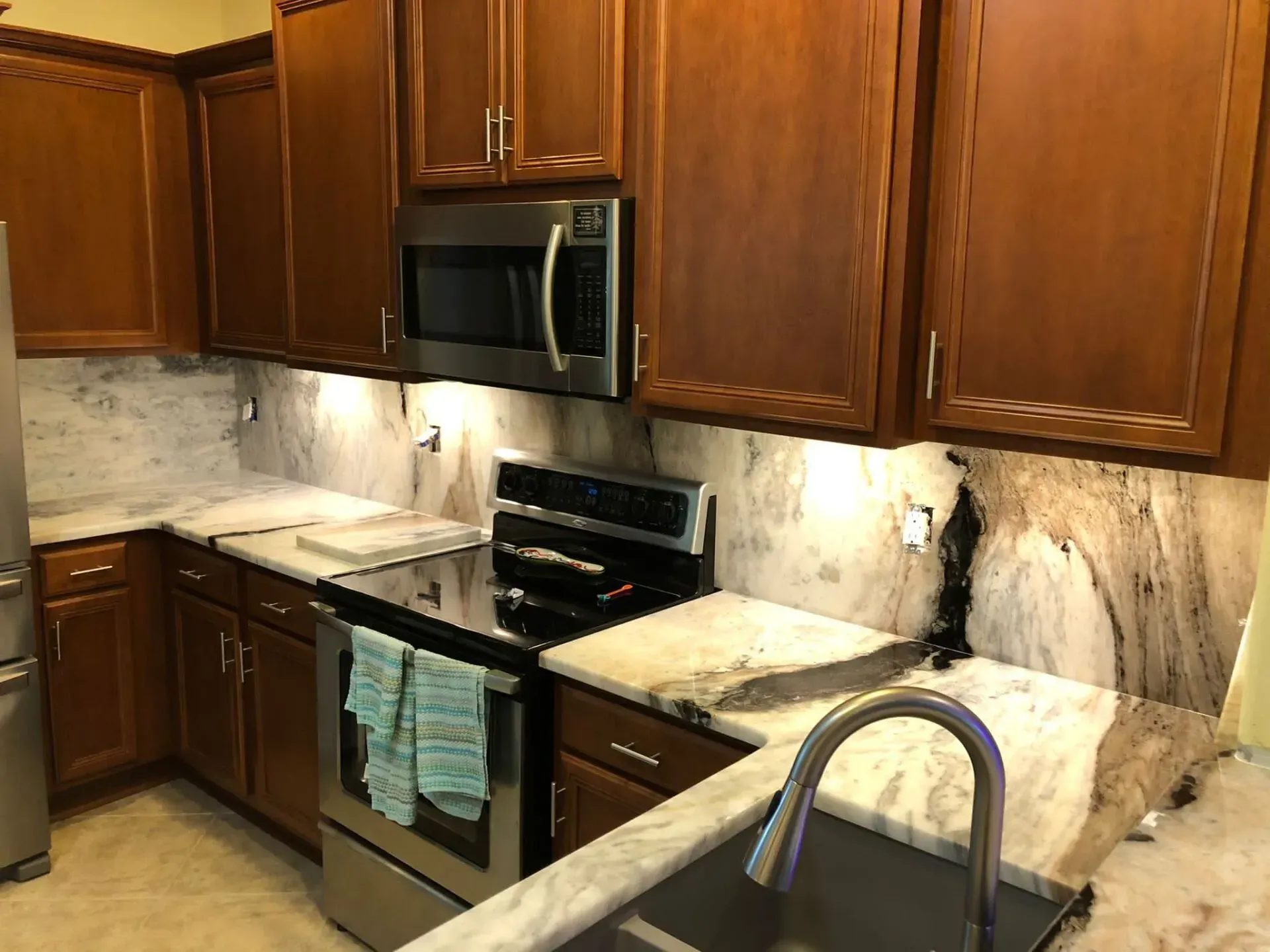 Wooden kitchen with stainless appliances, marble countertops, and a sink in the foreground