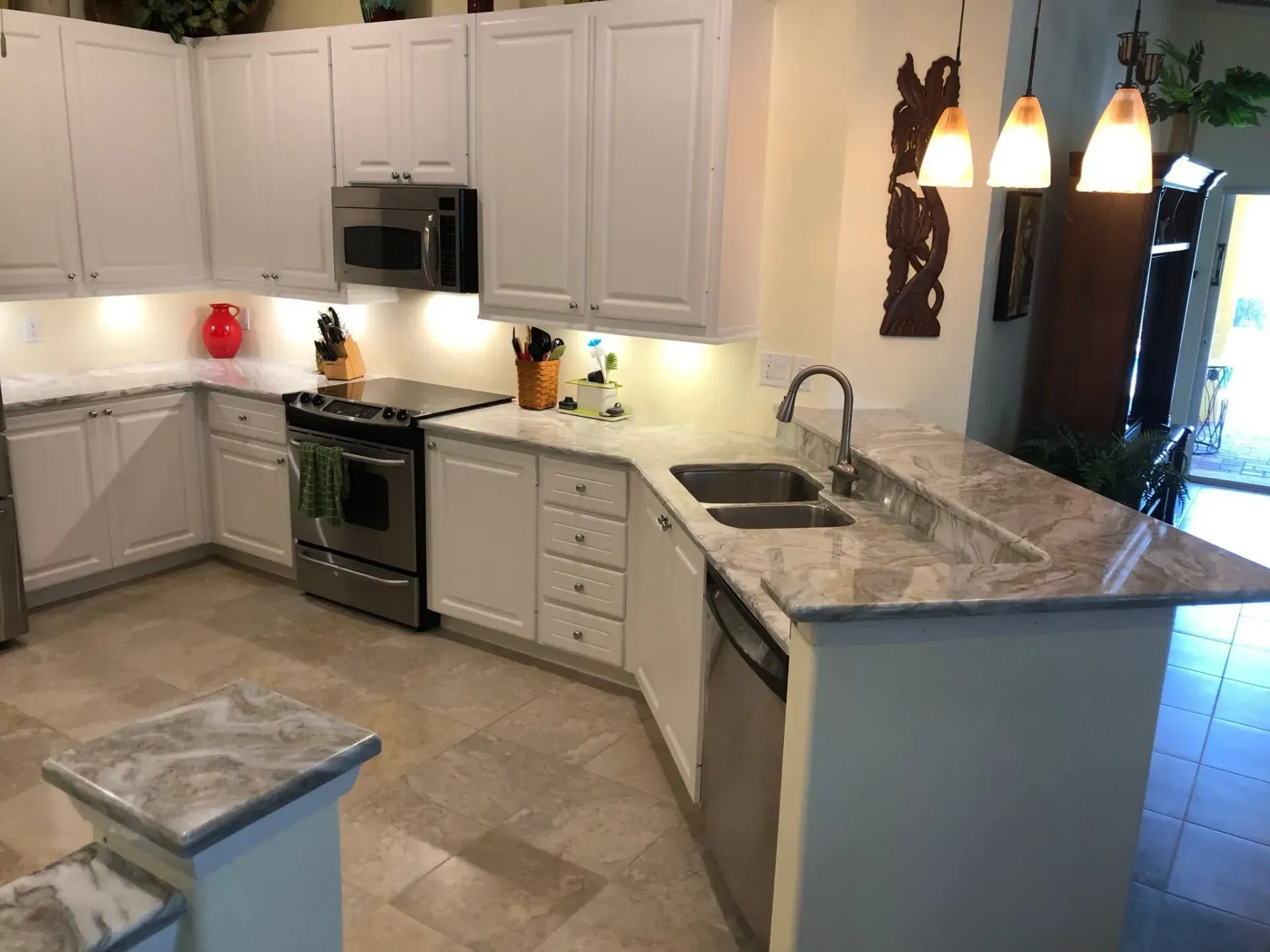 Modern kitchen with white cabinets, stainless stove, marble island, and pendant lights