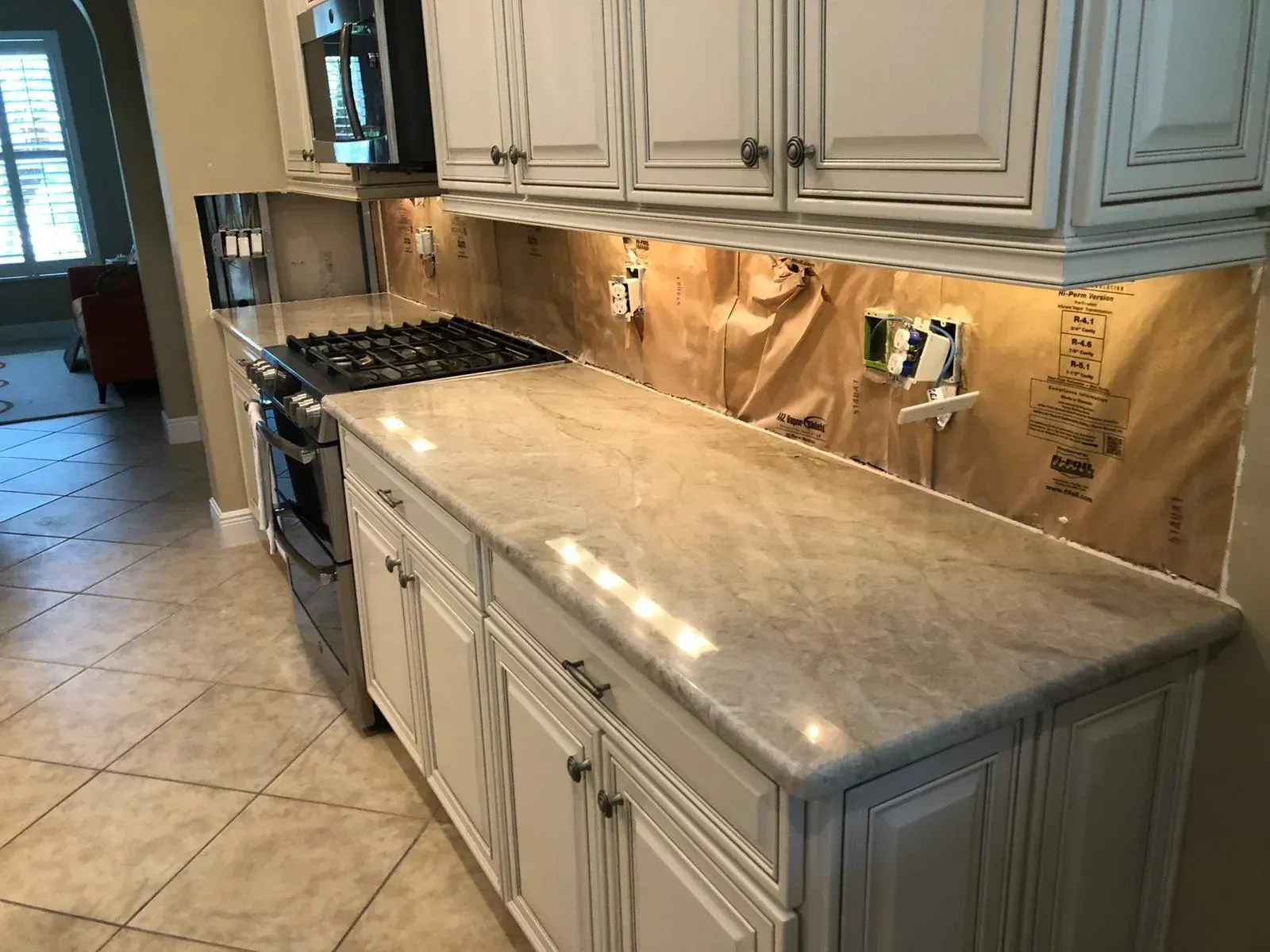 Kitchen with gray cabinets, tan tile backsplash, black stove, and long light granite countertop.