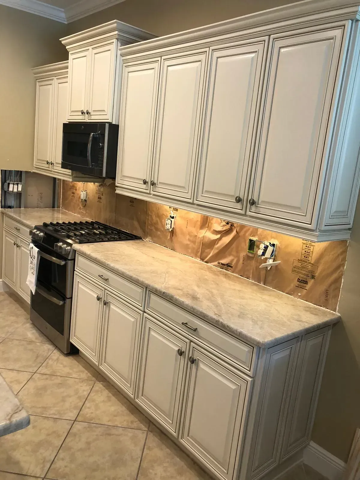 White kitchen with ornate cabinets, granite counters, stainless stove, and beige tile floor