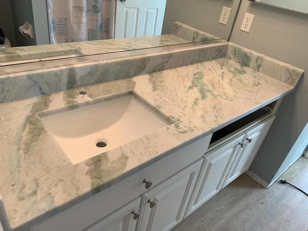 White marble bathroom vanity with single sink, large mirror, and white cabinet doors under the counter.