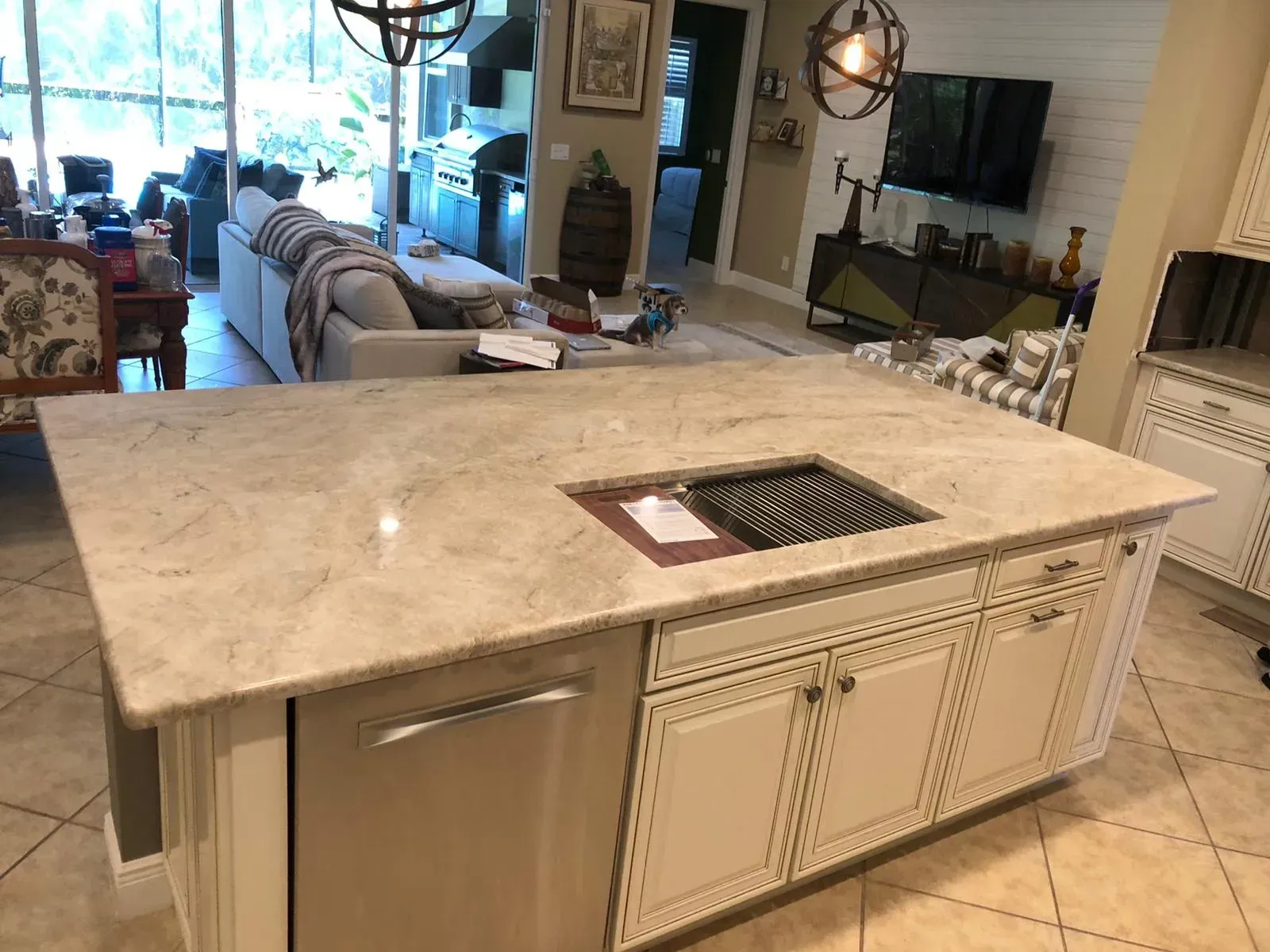 Kitchen island with beige marble countertop and sink, viewed from a living room interior.