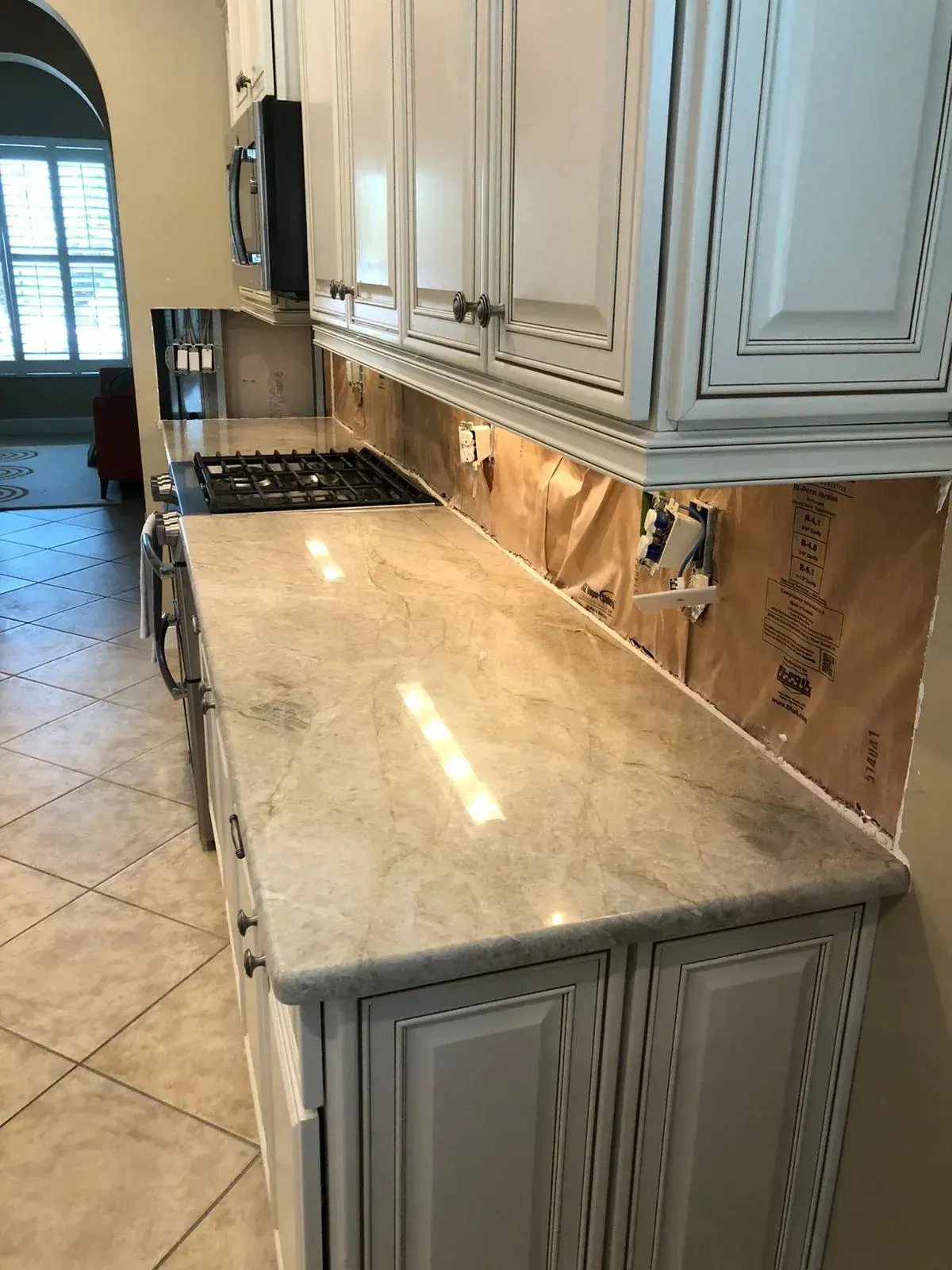 Kitchen countertop with white cabinets, marble surface, gas cooktop, and tiled floor.