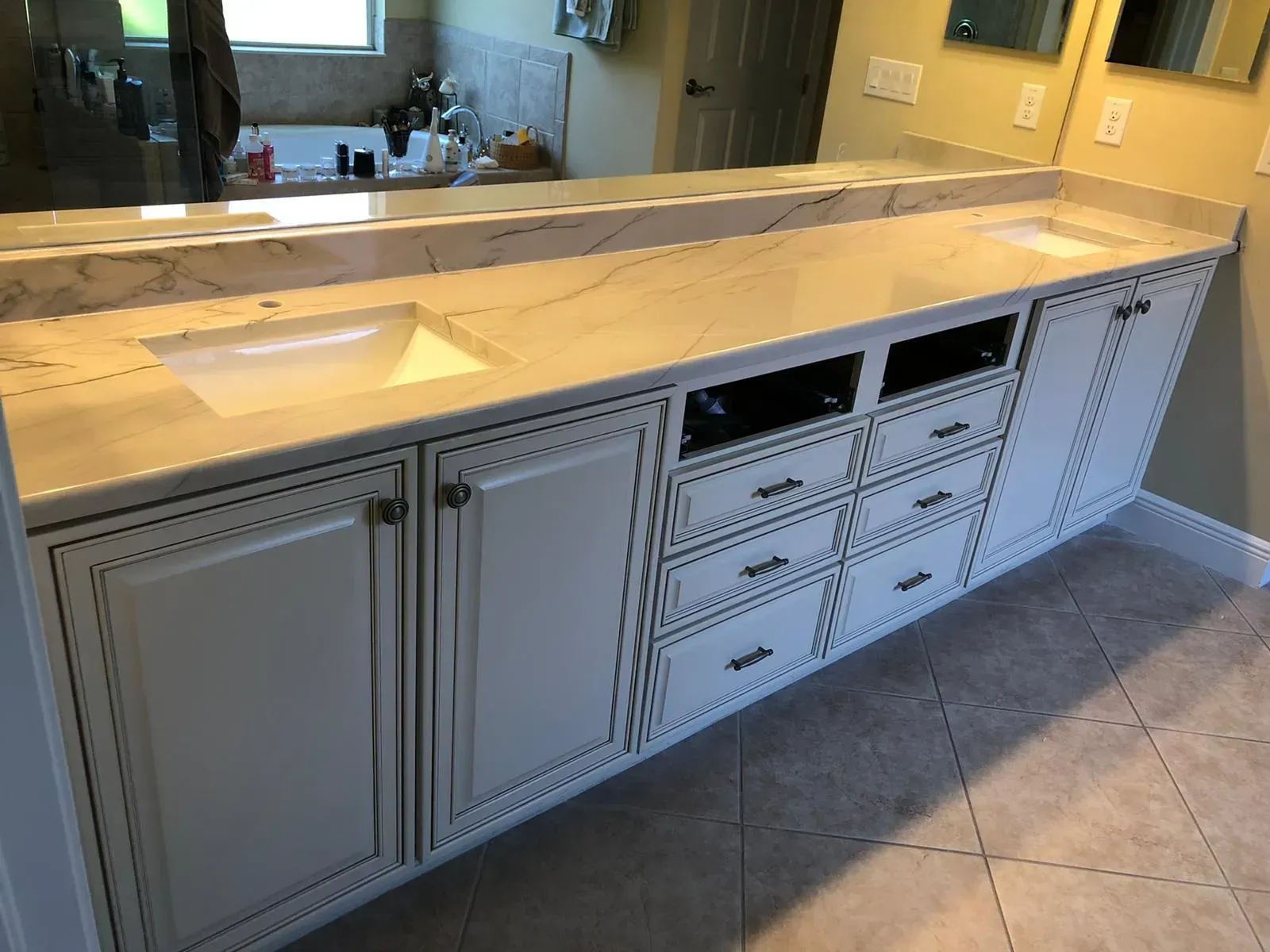 Long white bathroom vanity with double sinks, drawers, and large mirror above tiled floor.