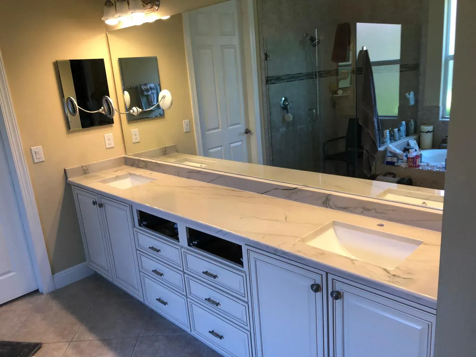 Bathroom vanity with double sinks, large mirror, and light wood cabinetry under warm lighting