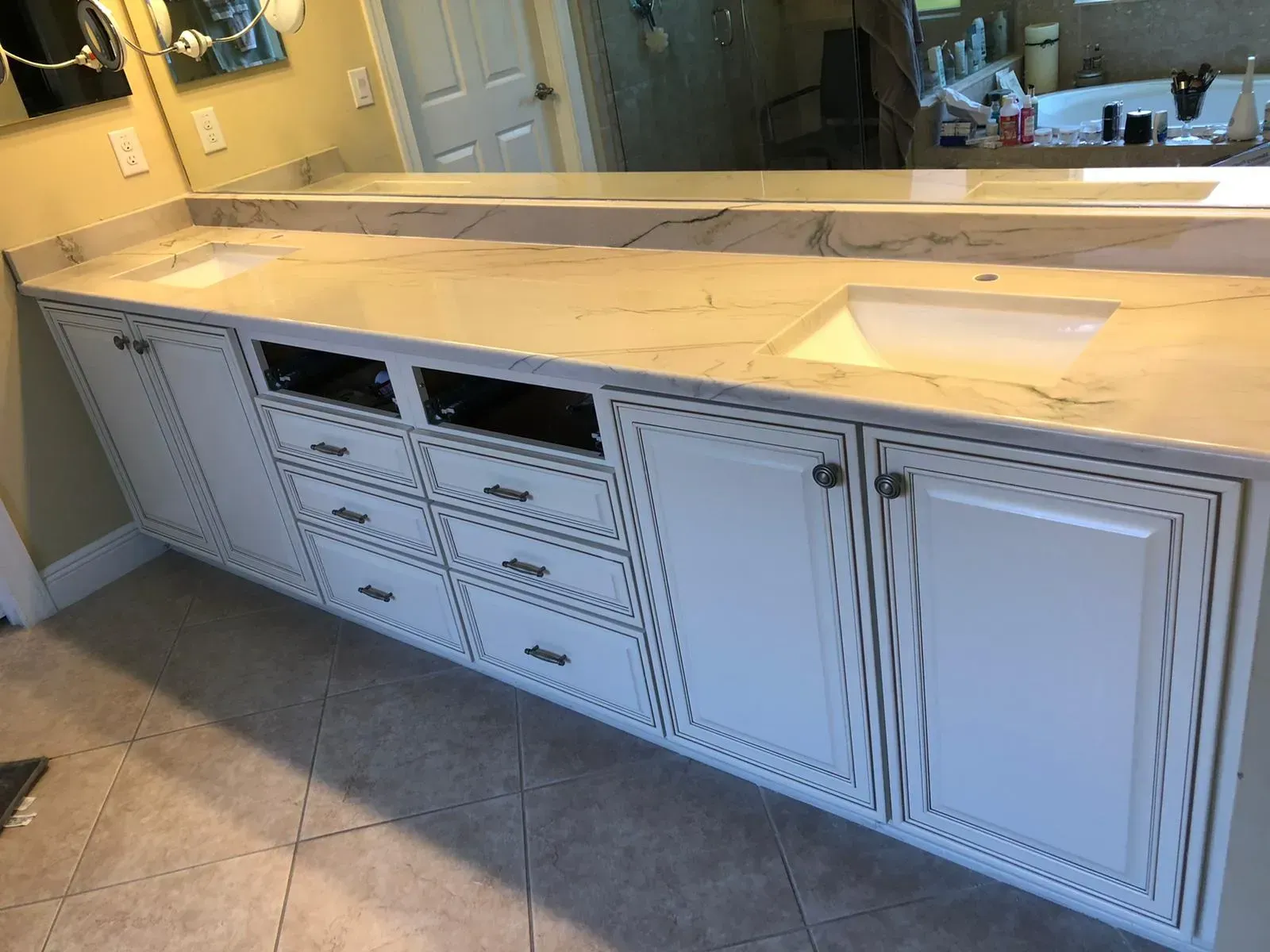 White bathroom vanity with double sinks, drawers, and cabinet doors beneath a large mirror.