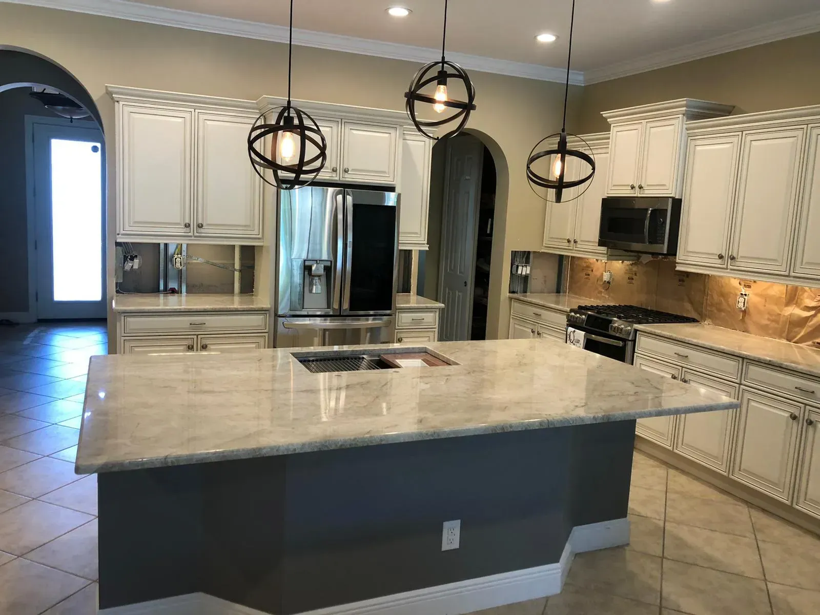 Modern kitchen with large marble island, stainless steel appliances, white cabinets, and hanging pendant lights