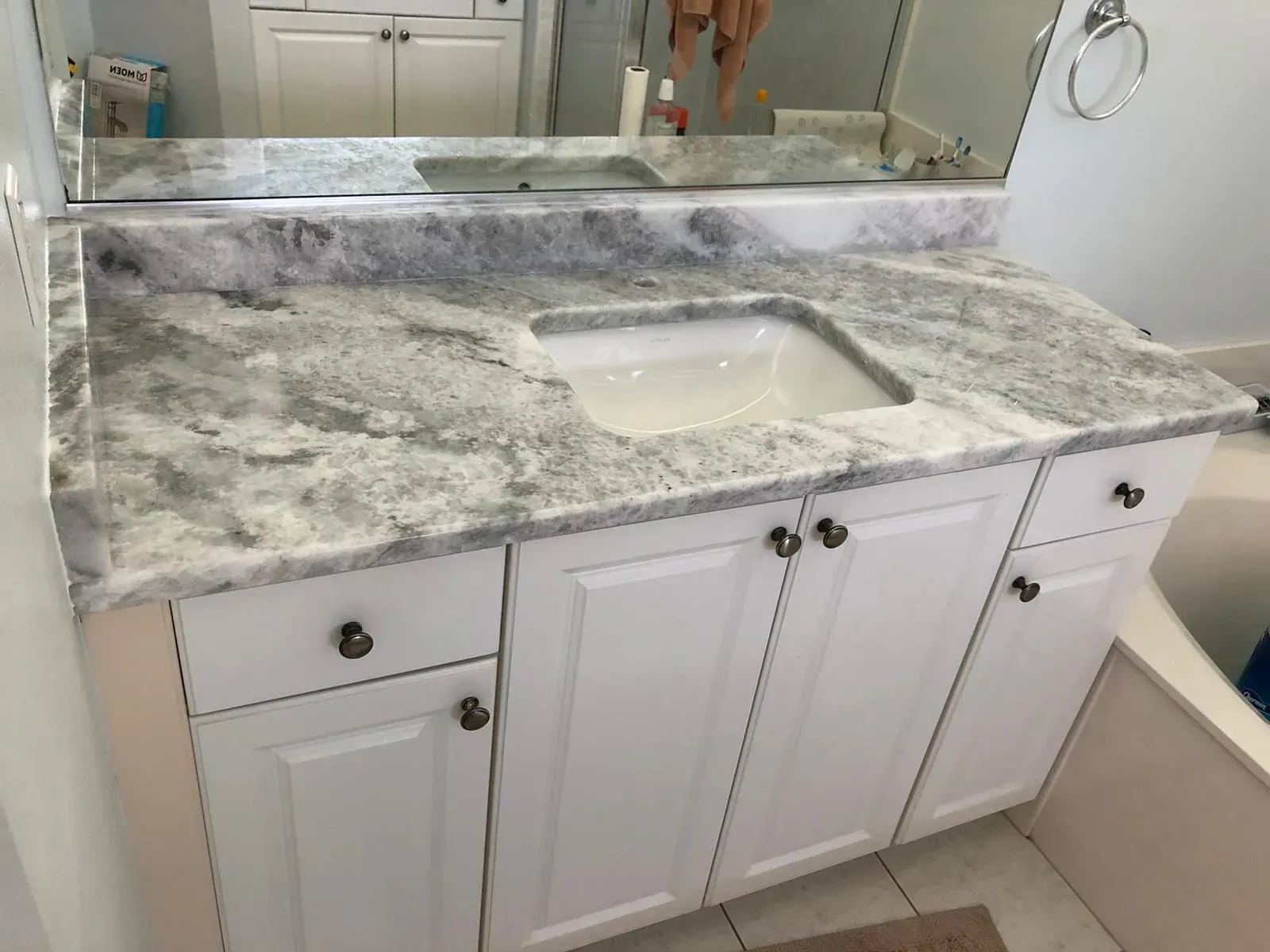 White bathroom vanity with marble-look countertop and sink, shown in front of a mirror.