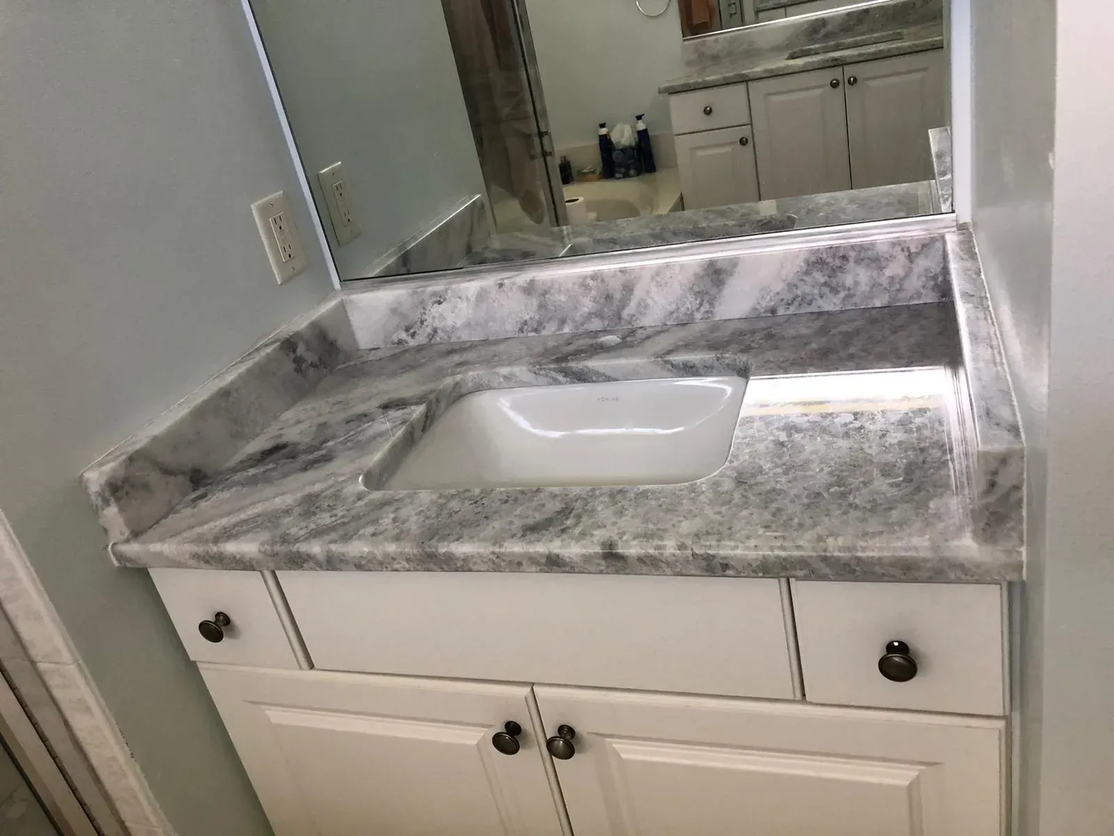 Bathroom vanity with white cabinets, gray marble countertop, sink, and large mirror