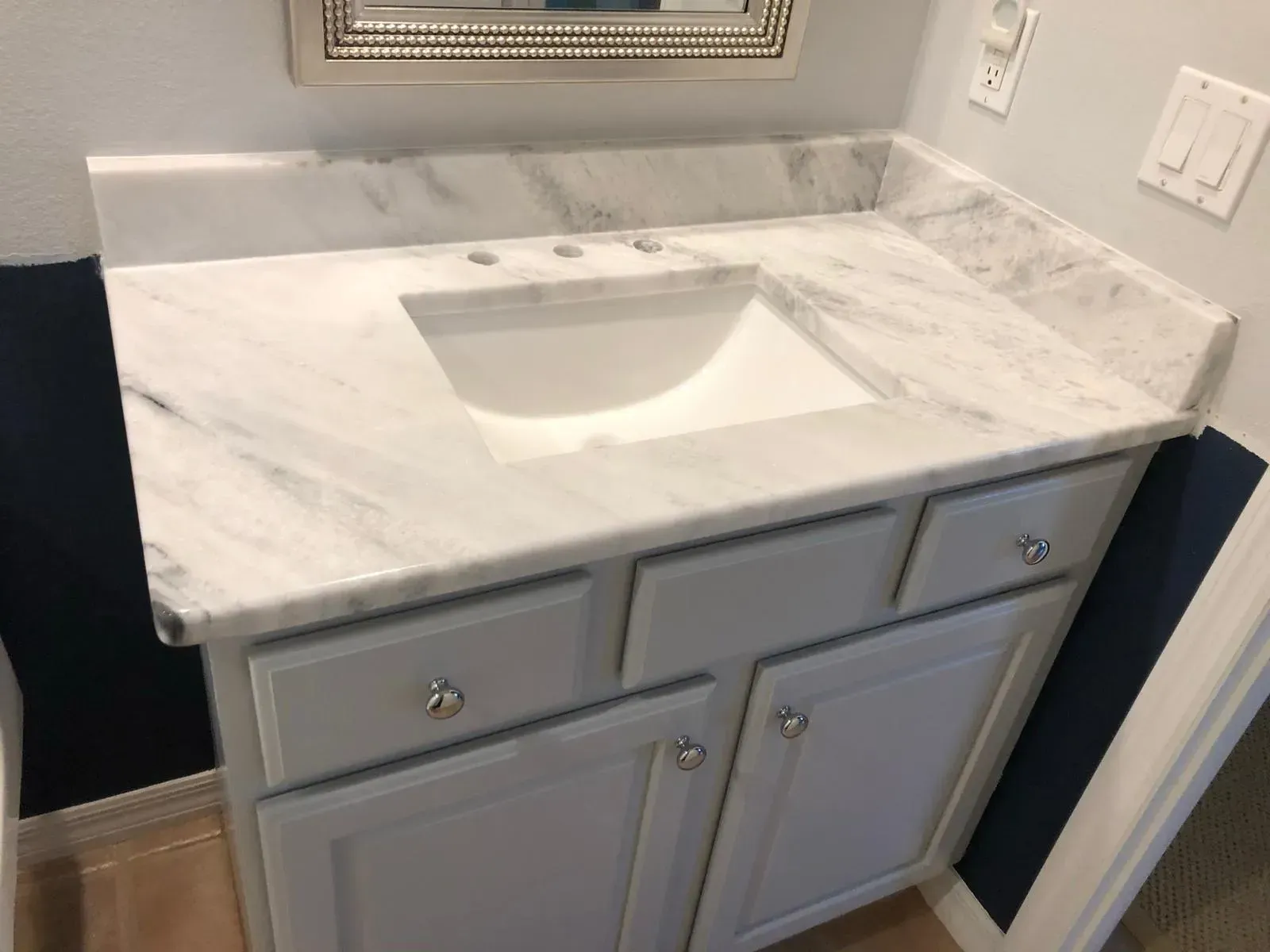White marble bathroom vanity with built-in sink and gray cabinet drawers beneath a mirror.