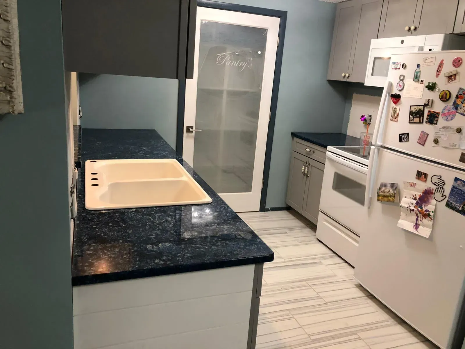 Small kitchen with blue countertops, white cabinets, stove, fridge, and a sink by a frosted-glass door.