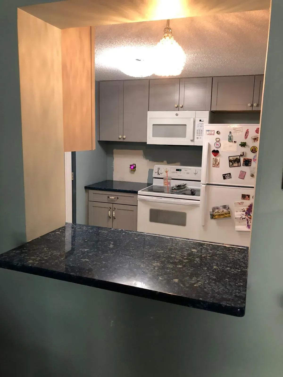 View into a small kitchen with white appliances, dark countertops, and a hanging light fixture