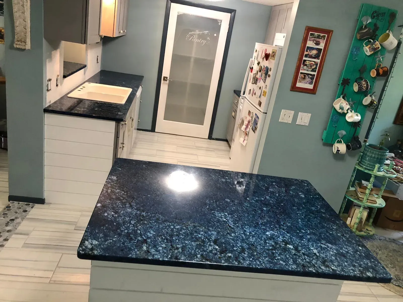 Modern kitchen with light blue cabinets, white tile floor, and a large blue galaxy-pattern island counter.