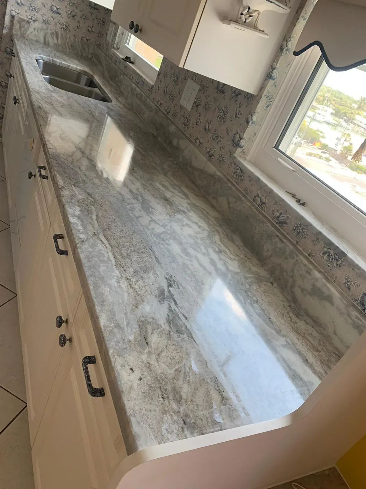 Modern kitchen with long marble countertop, sink, white cabinets, and window light