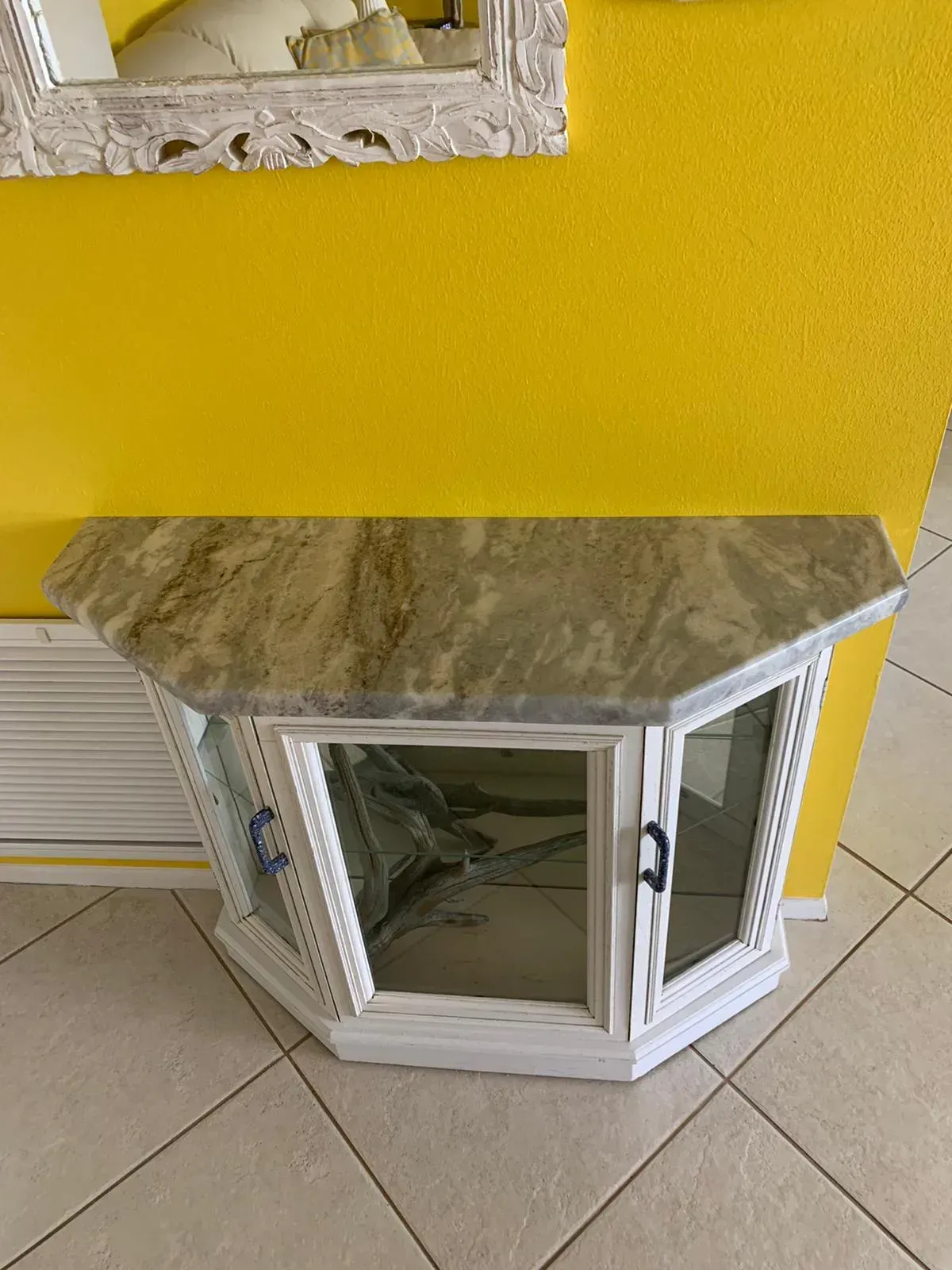 White cabinet with marble top against a bright yellow wall on a tiled floor