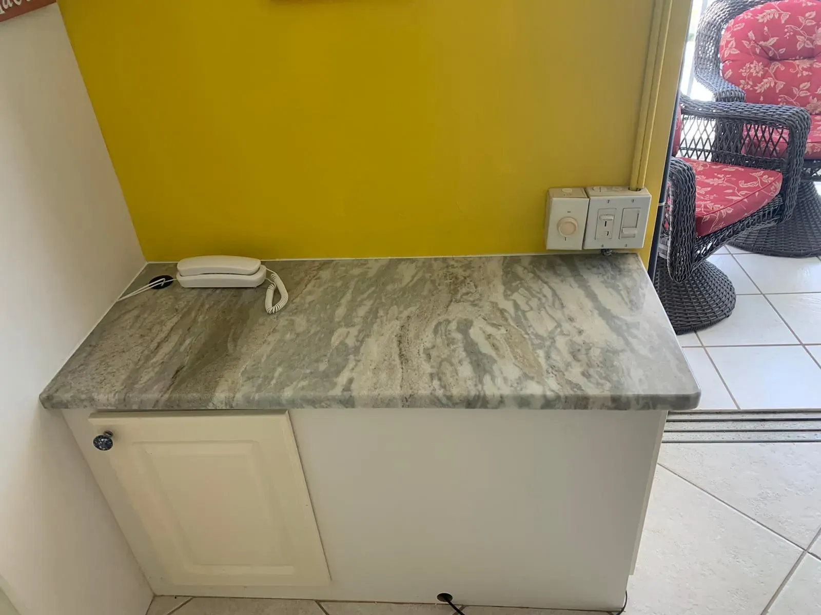 Small countertop cabinet with gray marble top against a yellow wall, holding a white iron and power cord.