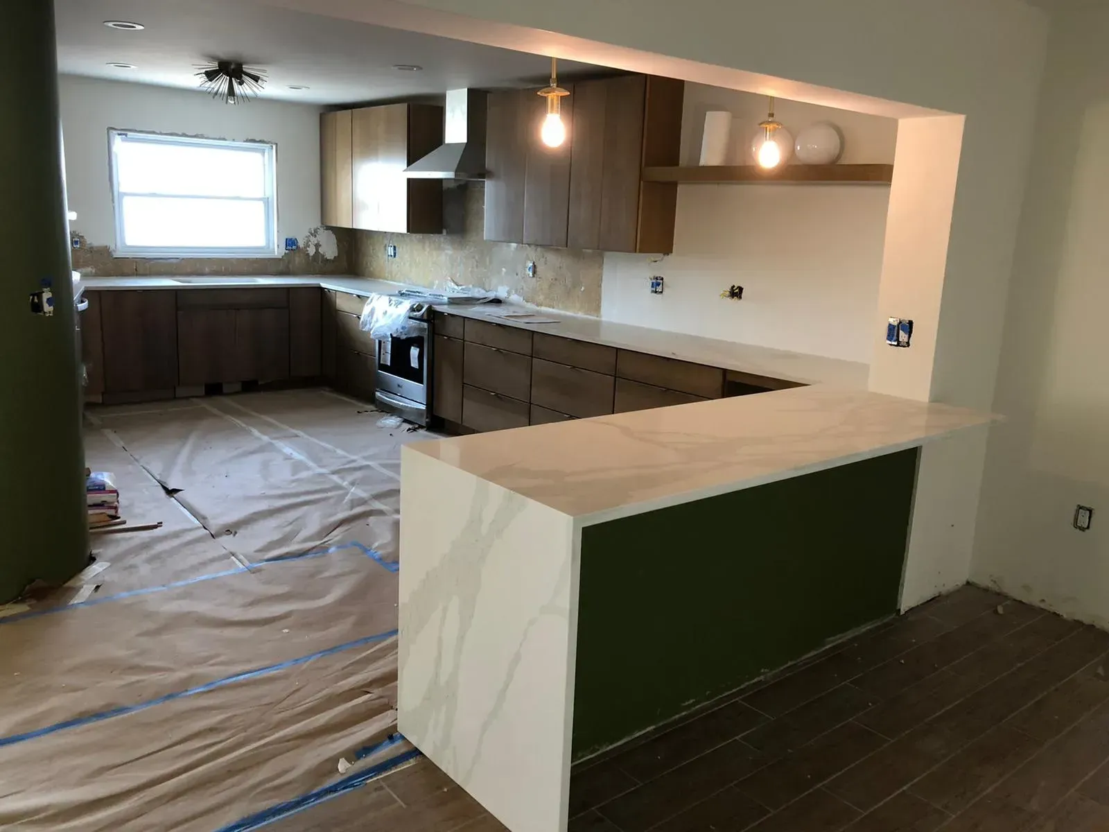 Kitchen renovation in progress with dark wood cabinets, white countertop, and floor covered in protective plastic.