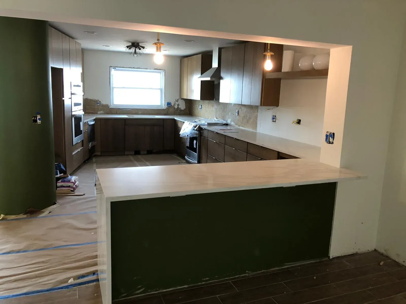 Kitchen under renovation with green island, white counters, unfinished floor, and exposed fixtures.