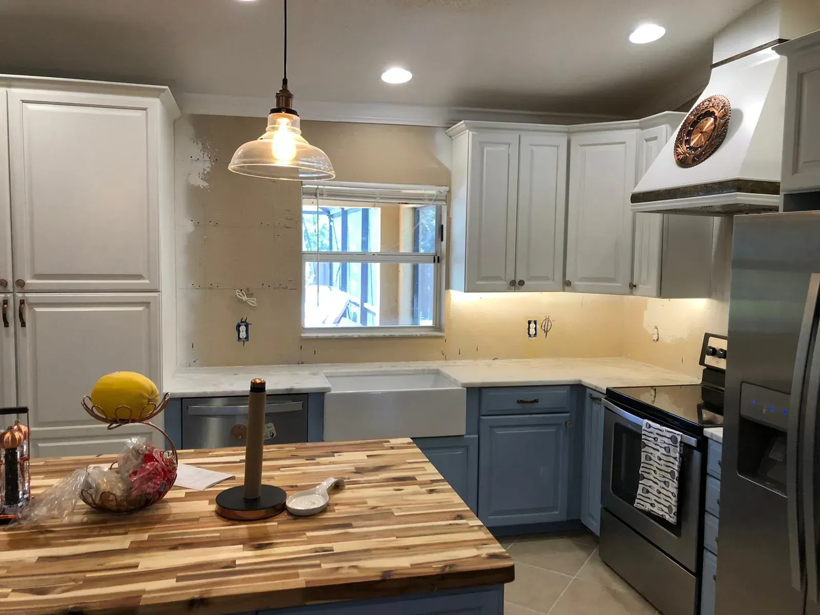 Modern kitchen with white cabinets, blue lower cabinets, island, pendant light, and stainless steel appliances