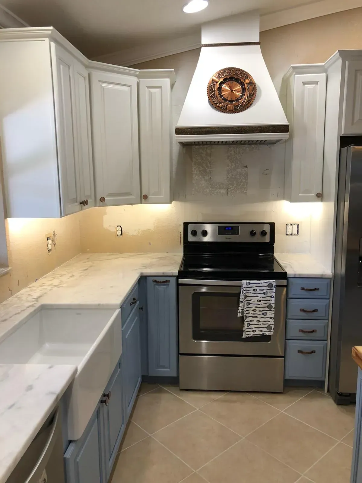 Modern kitchen with white cabinets, marble counters, stainless stove, and tiled floor.