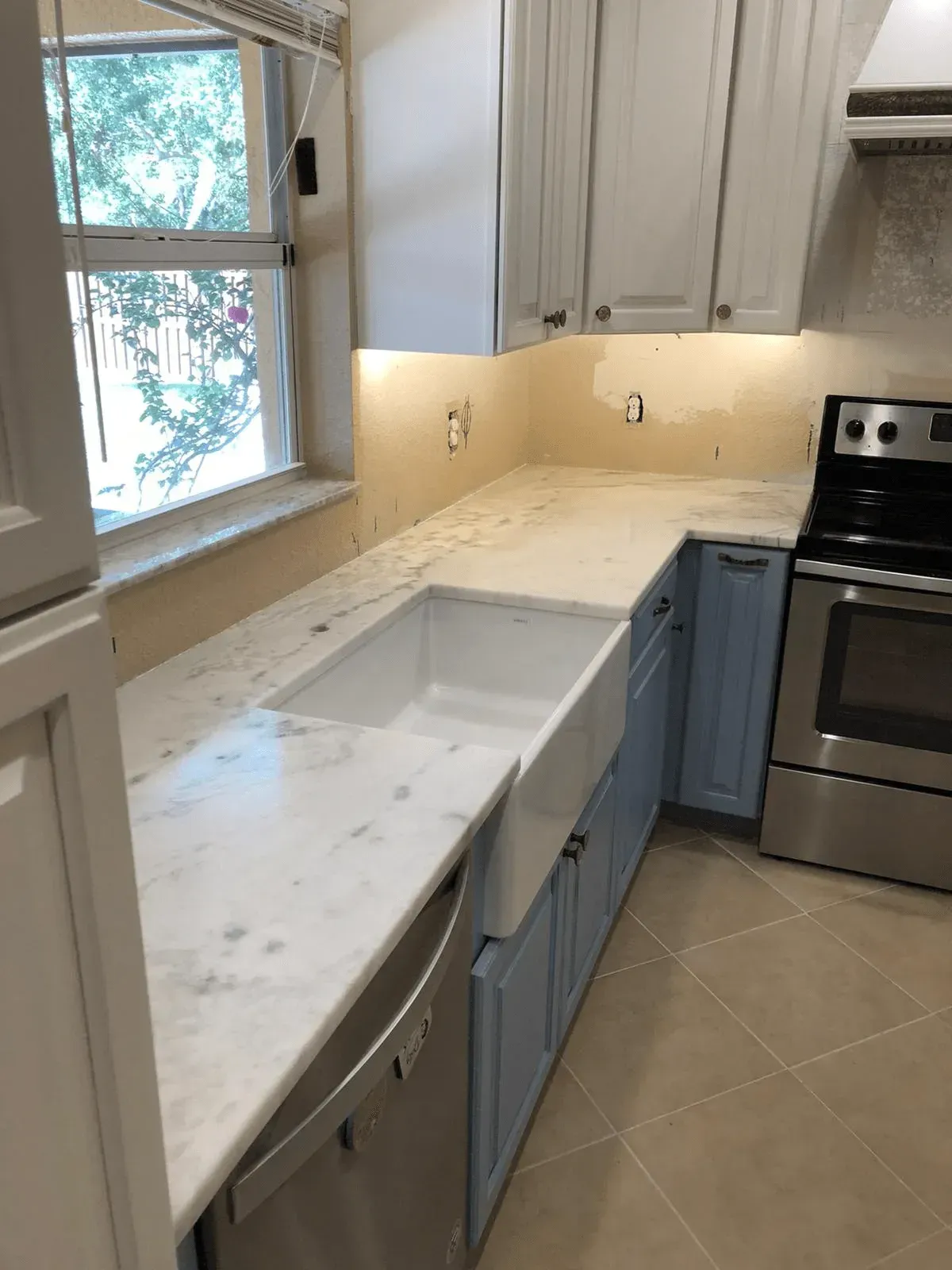 Bright kitchen with white cabinets, marble countertop, sink by window, and stainless steel oven.