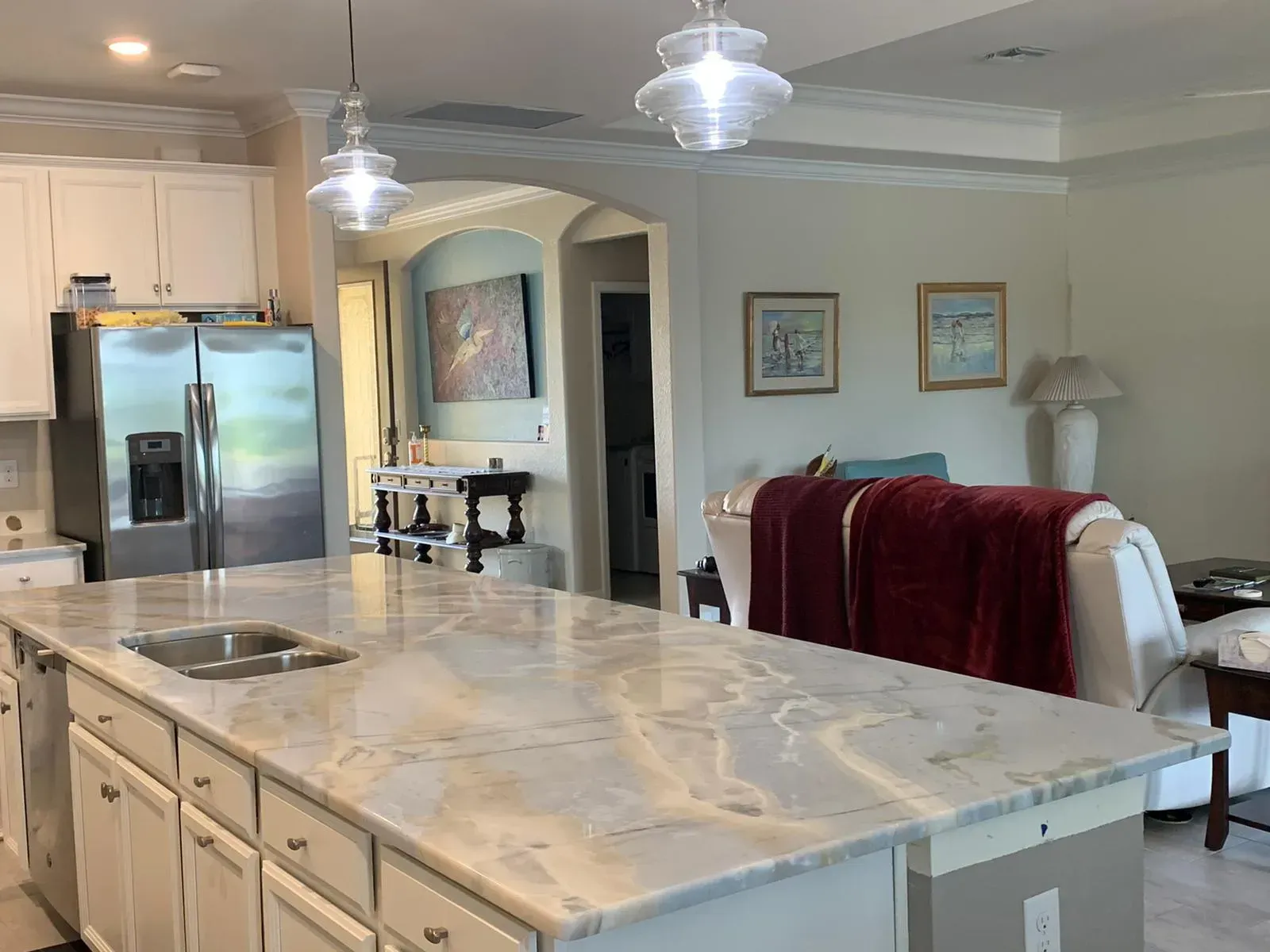 Bright kitchen with marble island, white cabinets, stainless fridge, and pendant lights