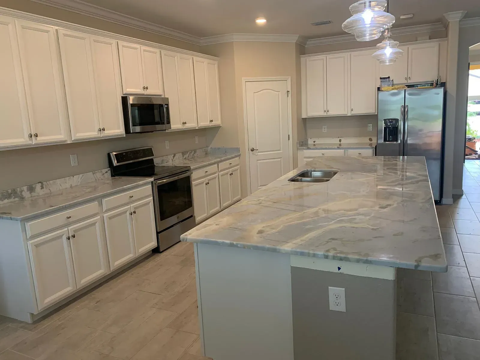 Bright kitchen with white cabinets, stainless appliances, and a large marble island