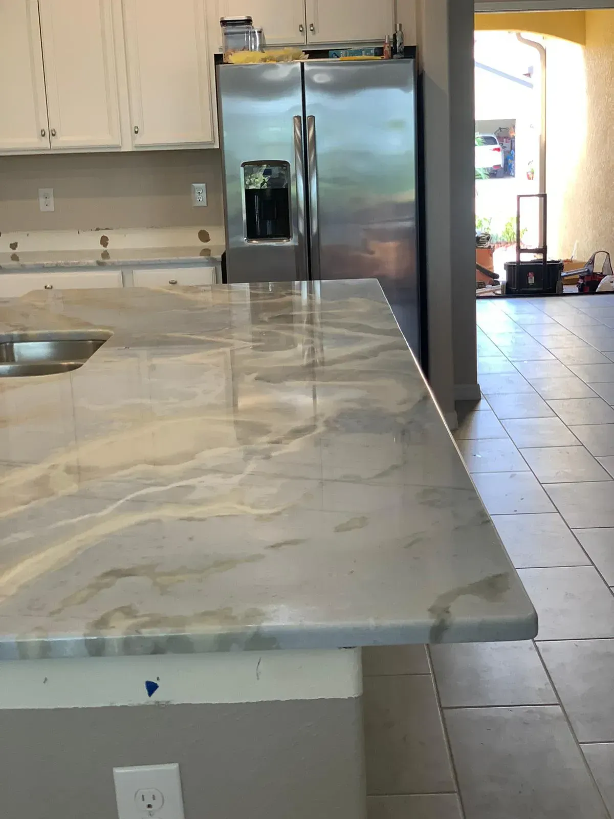 Kitchen with marble island countertop and stainless steel refrigerator beside tiled floor entryway