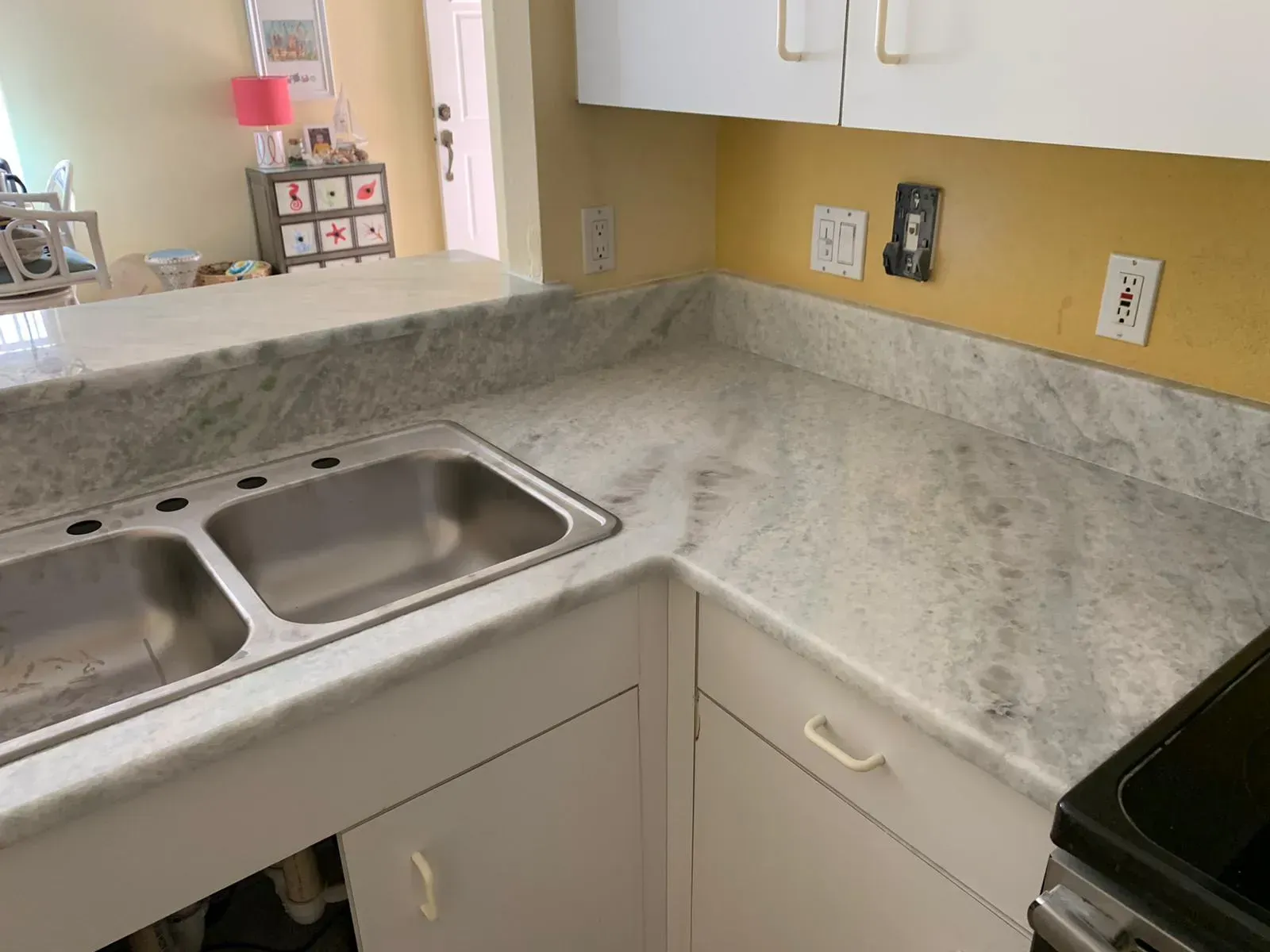 Kitchen corner with double sink, speckled countertop, and tan backsplash beside a stove.