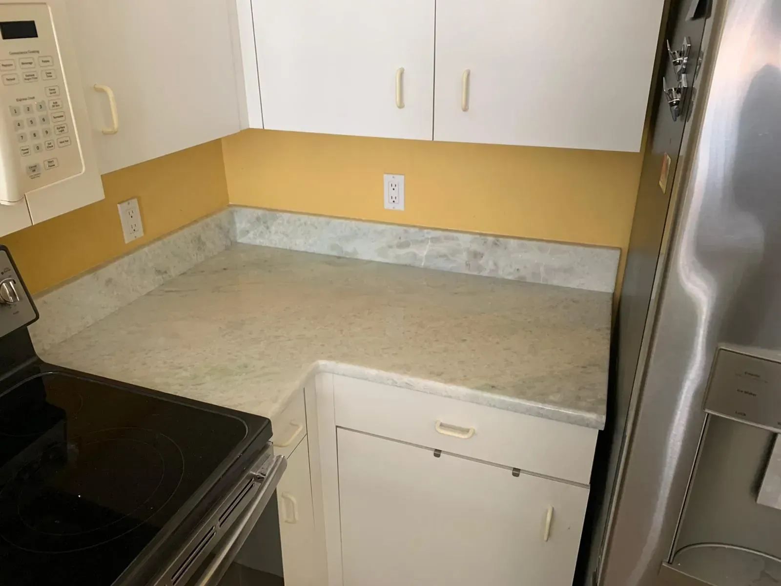 Kitchen corner with beige countertop, white cabinets, and stainless steel appliances next to a black stove.
