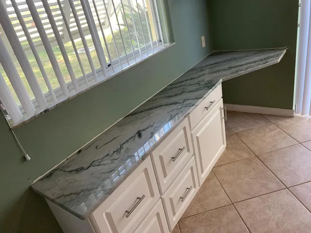 White cabinets with green marble countertop in a tiled room near a window with blinds.