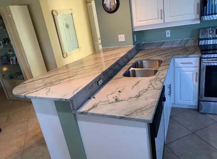 Kitchen island with marble-look countertops, a raised breakfast bar, and a sink in a bright white kitchen.