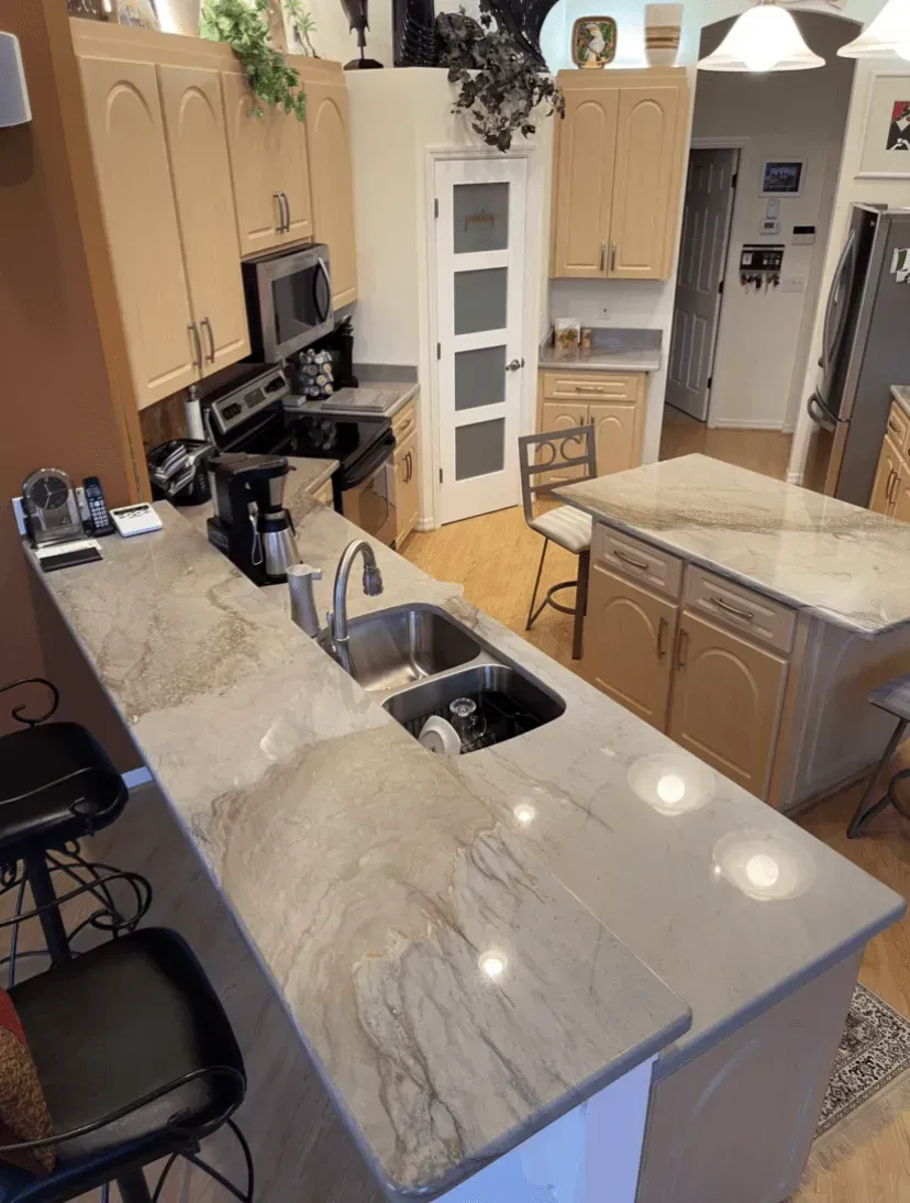 Modern kitchen with light wood cabinets, marble island, stainless sink, and black barstools