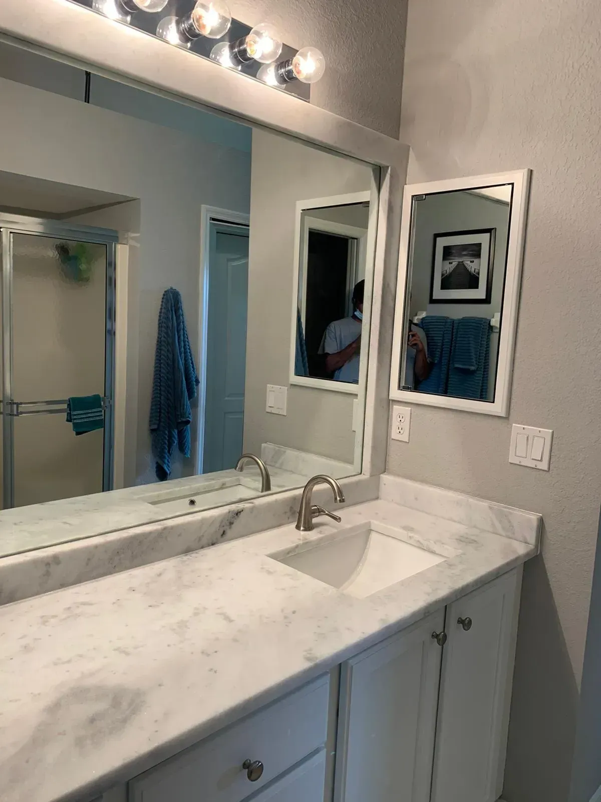 Modern bathroom vanity with white marble countertop, mirror, sink, and blue towels reflected in the mirror.