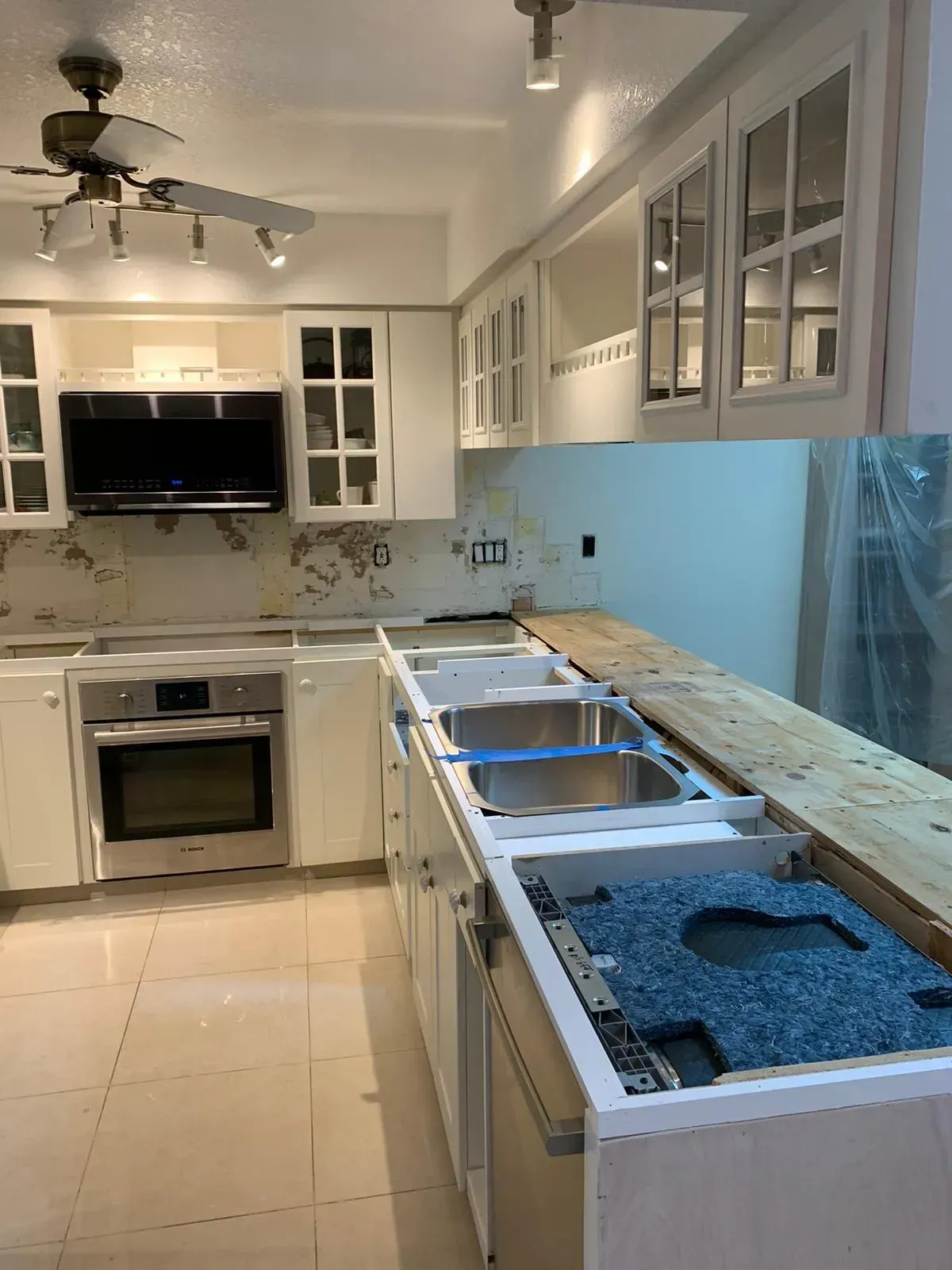 Modern white kitchen with built-in appliances, marble backsplash, and an unfinished countertop/ sink installation