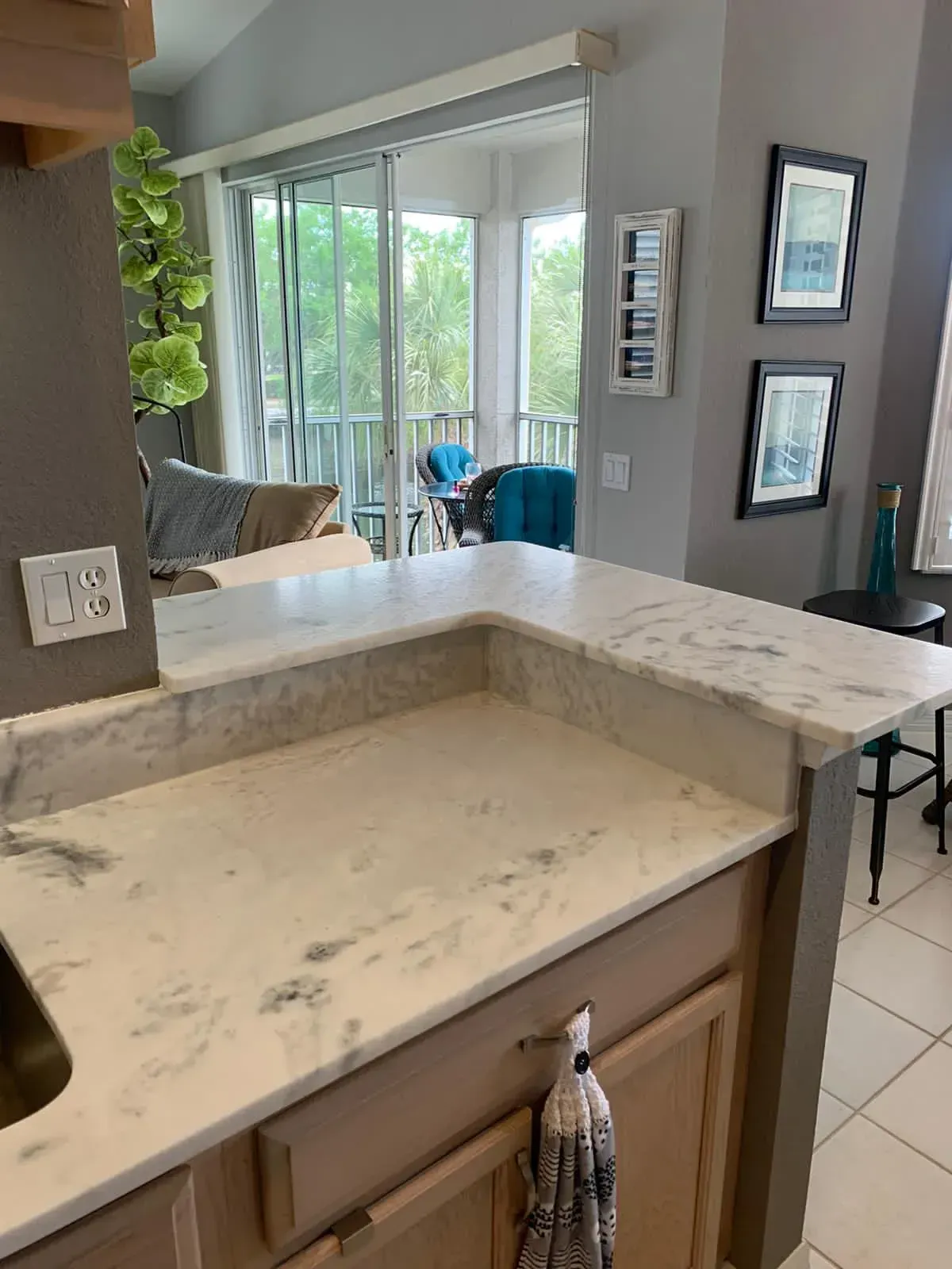 Kitchen countertop with marble island overlooking a bright living room and sliding glass doors.
