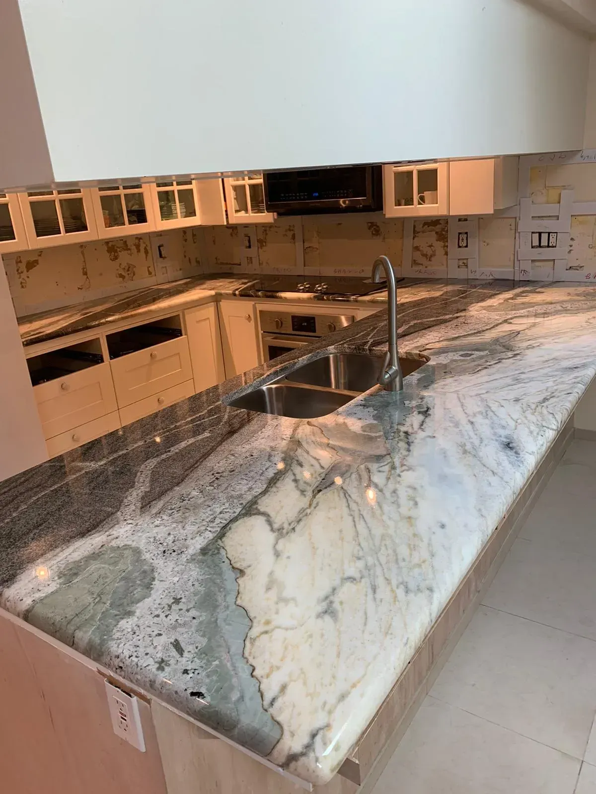 Modern kitchen with large gray-and-white marble island and stainless sink, open cabinets, and tile backsplash
