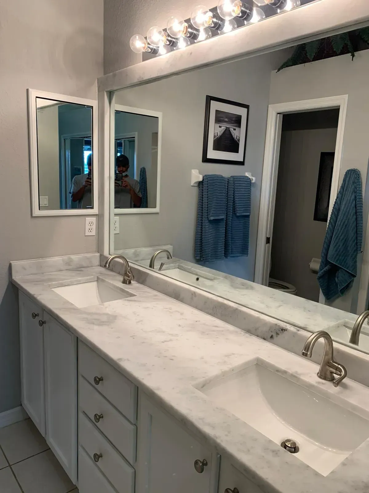 Bright bathroom vanity with marble countertop, large mirror, double sinks, and blue towels on the wall